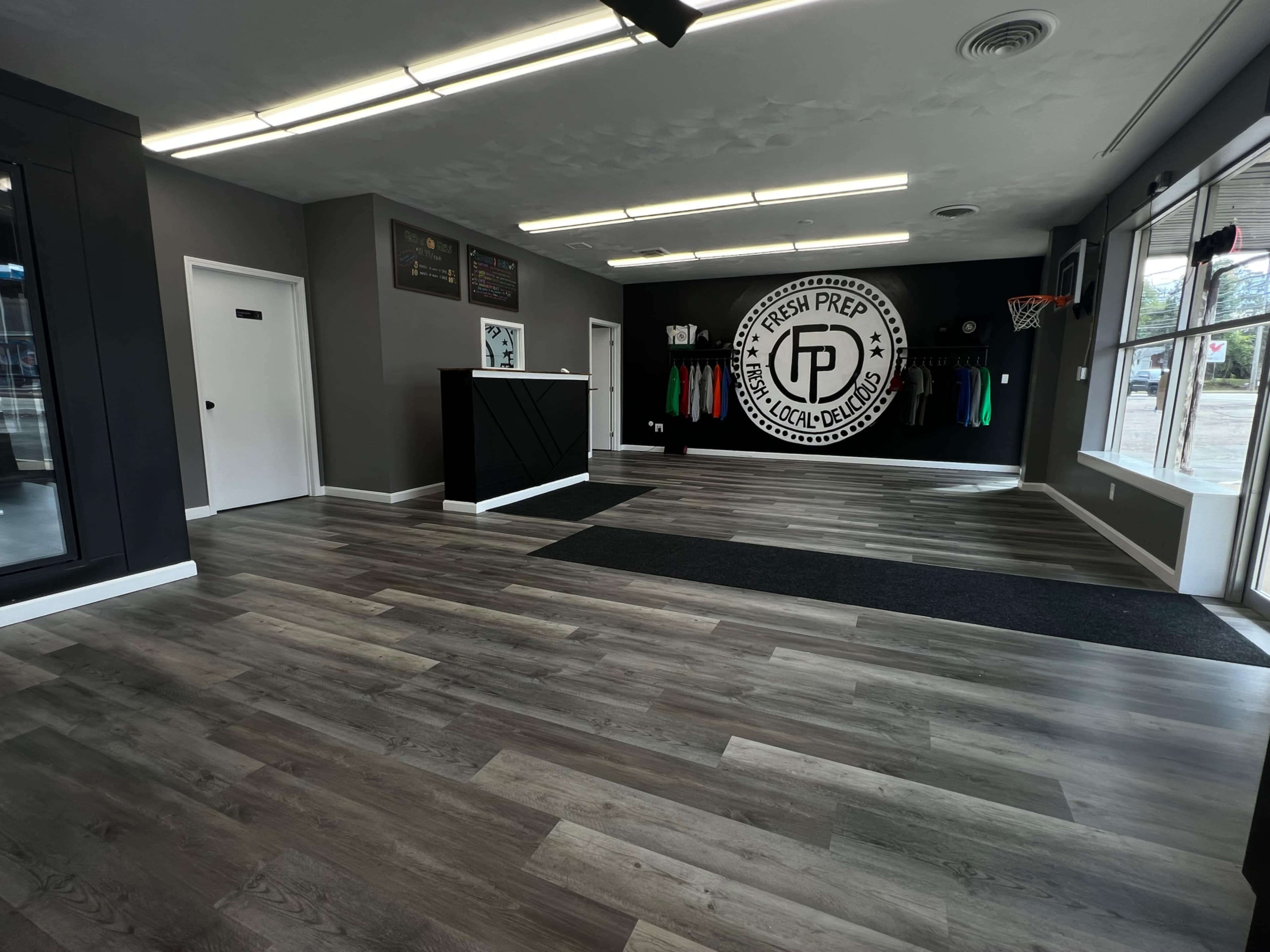 The interior of a retail space features gray walls, wooden flooring, a reception desk, and a wall logo, with clothing displayed and a small basketball hoop visible.