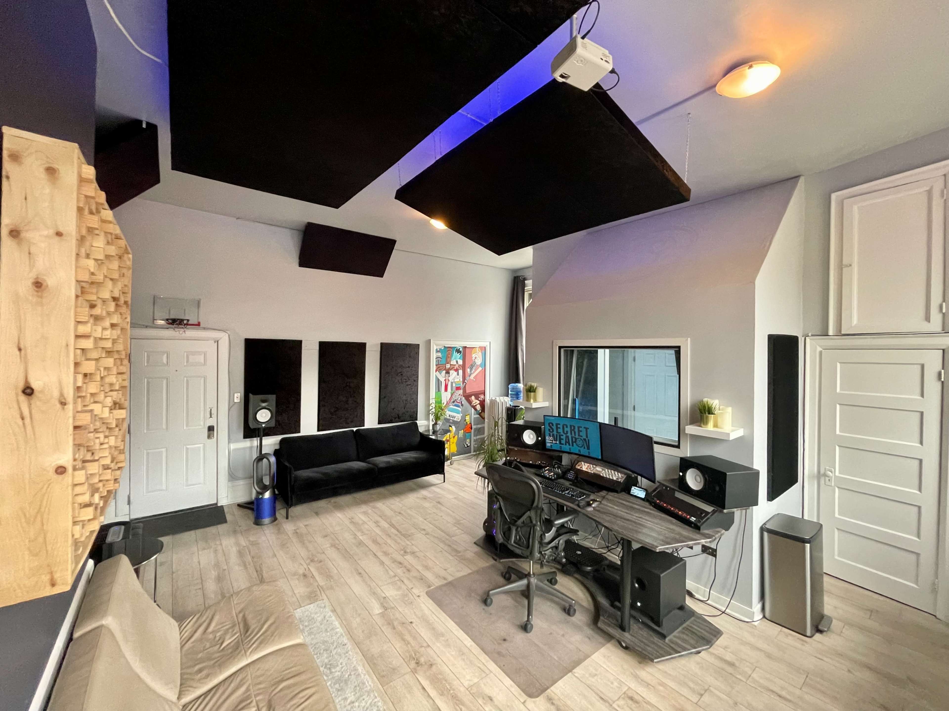A modern recording studio featuring a desk with audio equipment, a black couch, and soundproofing panels on the walls.