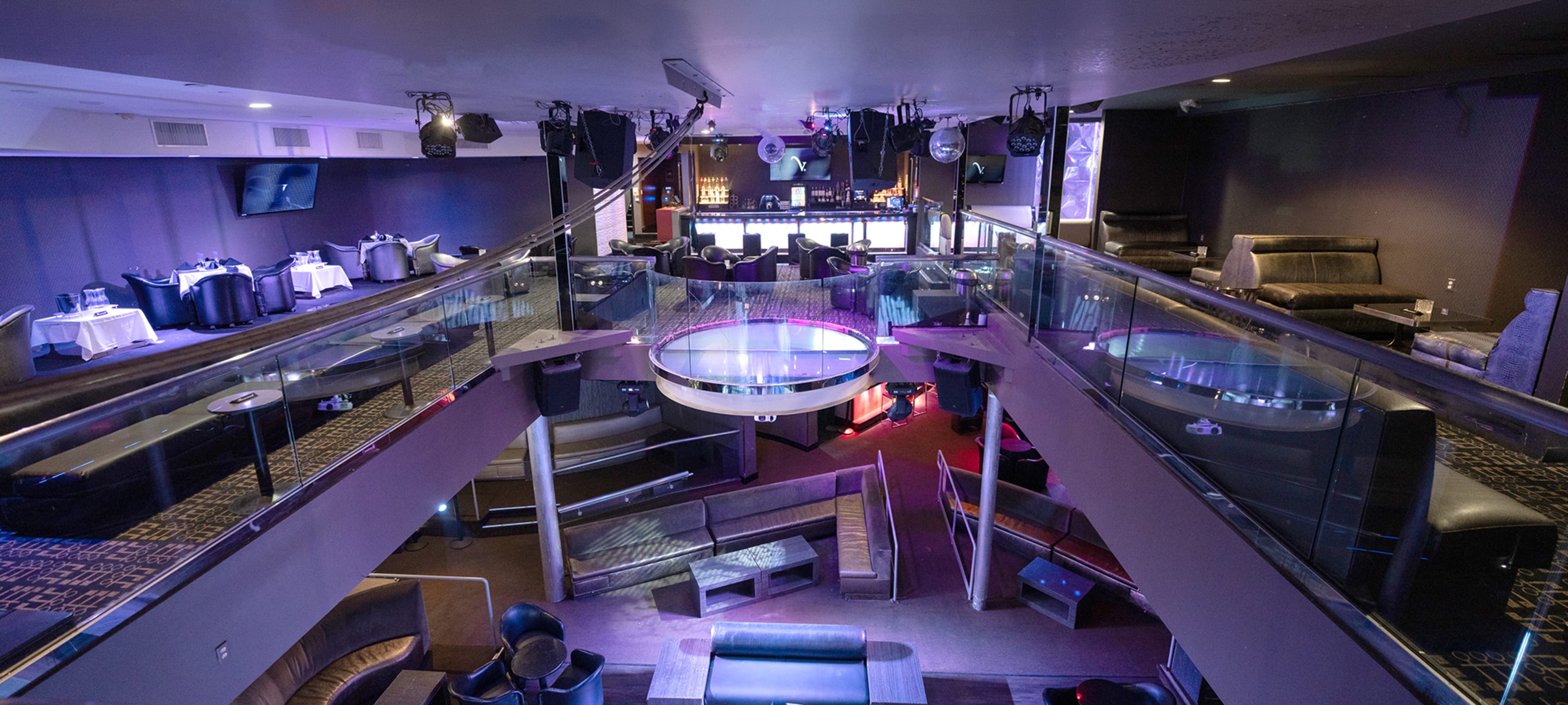 The image shows a spacious, multi-level lounge or nightclub with a bar area, various seating arrangements, and colorful lighting.