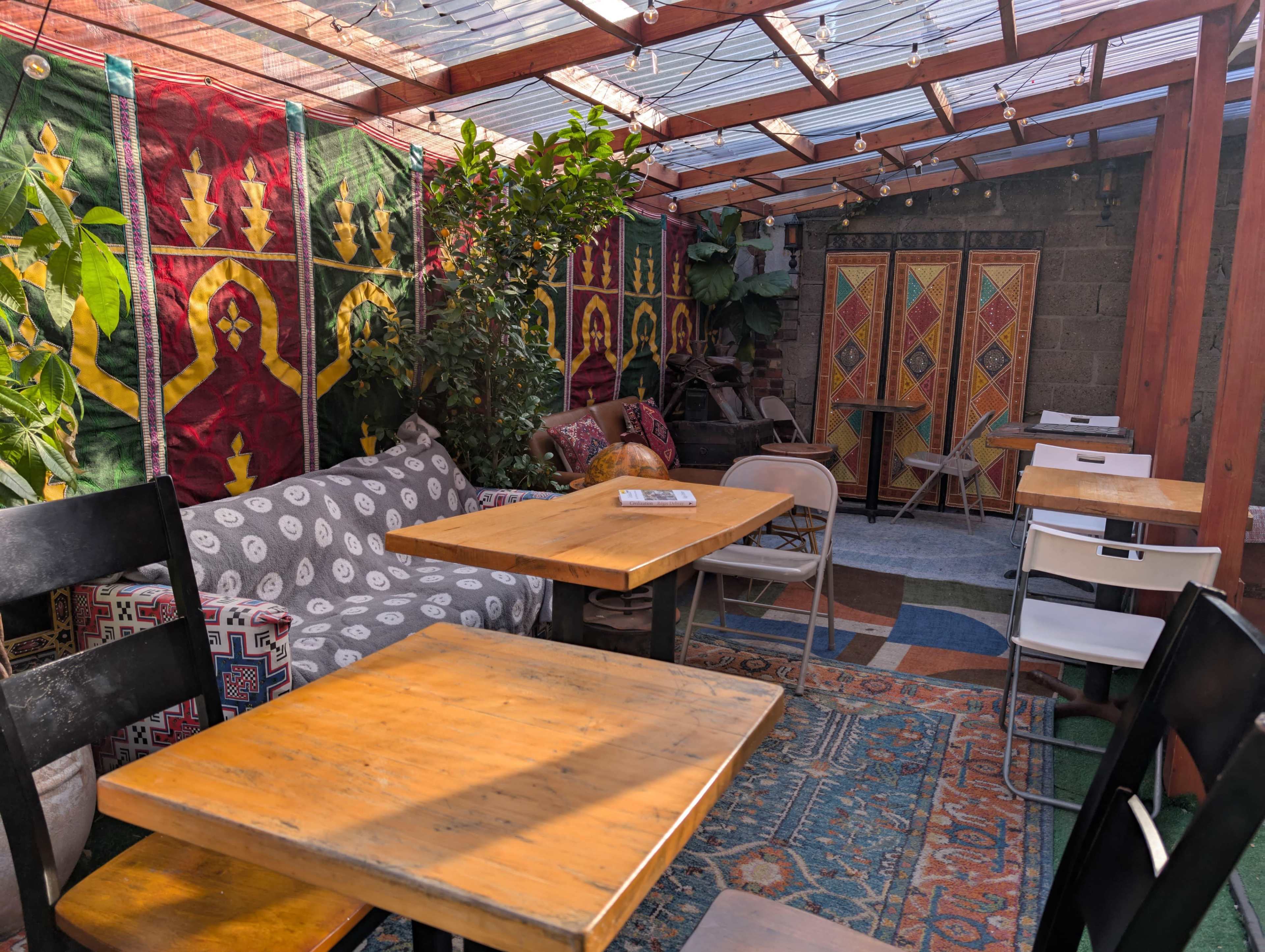 The image shows a colorful indoor garden cafe with wooden tables, patterned textiles on the walls, and various seating arrangements.