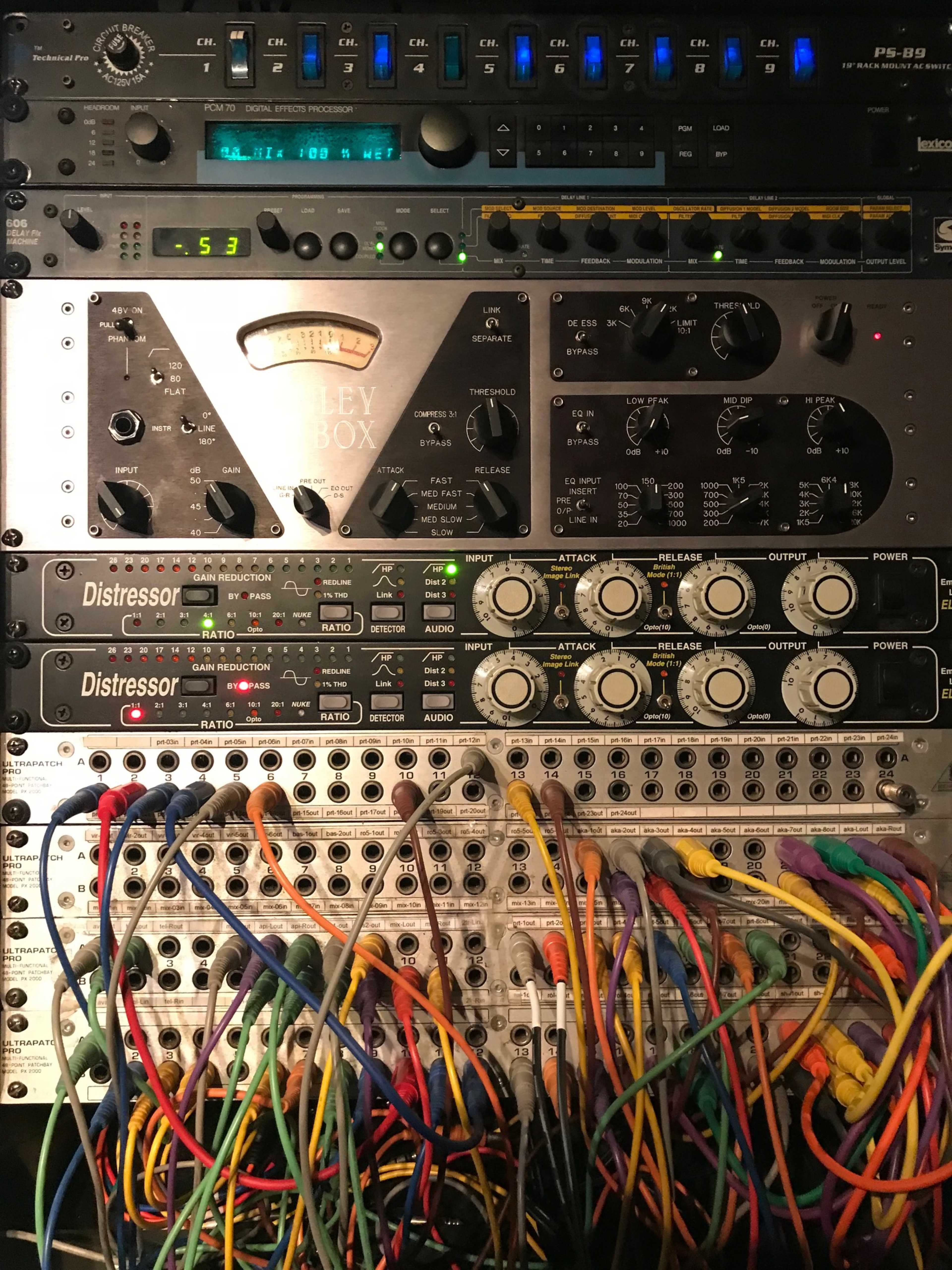 The image shows a stacked rack of audio equipment featuring various processors and patch cables integrated into a complex setup.