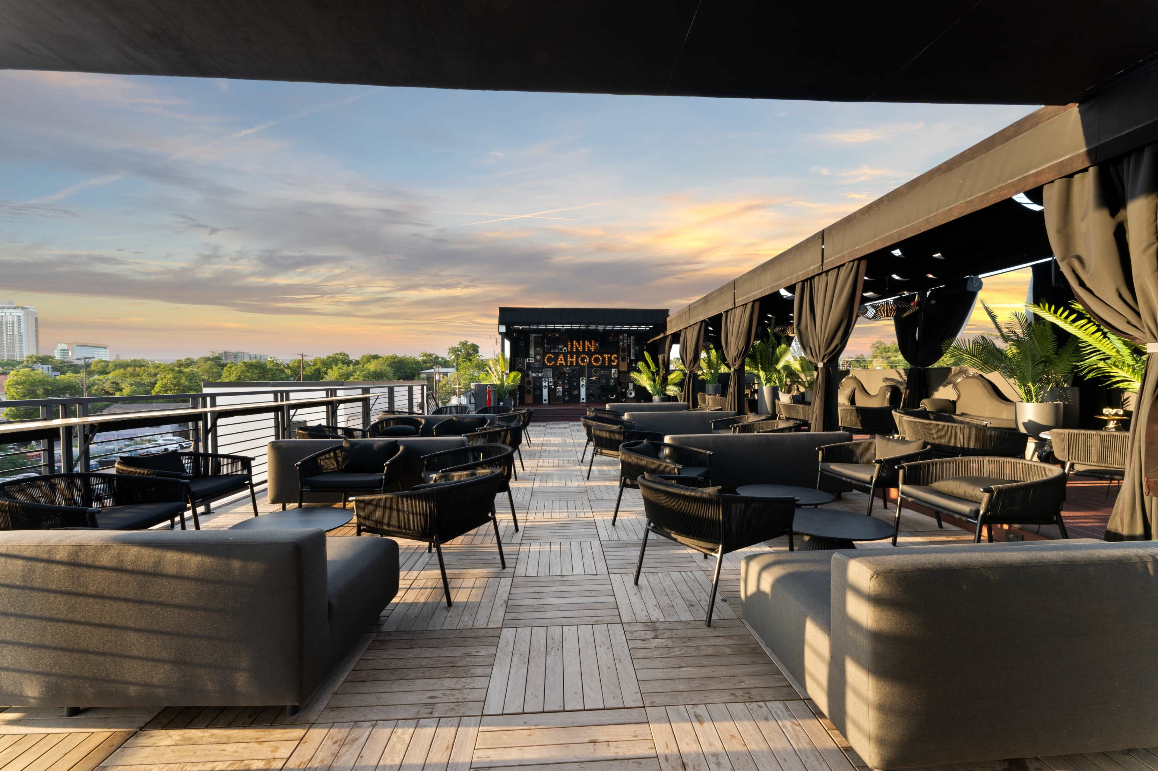 A rooftop lounge area with black furniture and a view of the skyline at sunset.