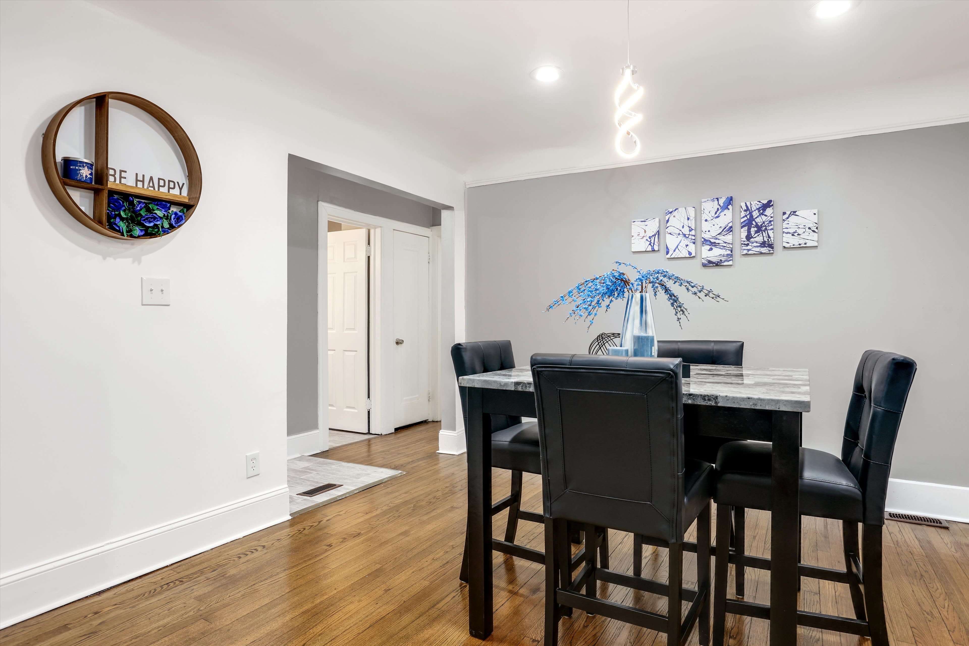 A modern dining area features a dark wood table surrounded by black chairs, with a decorative piece on the wall and a vase of blue flowers in the center.