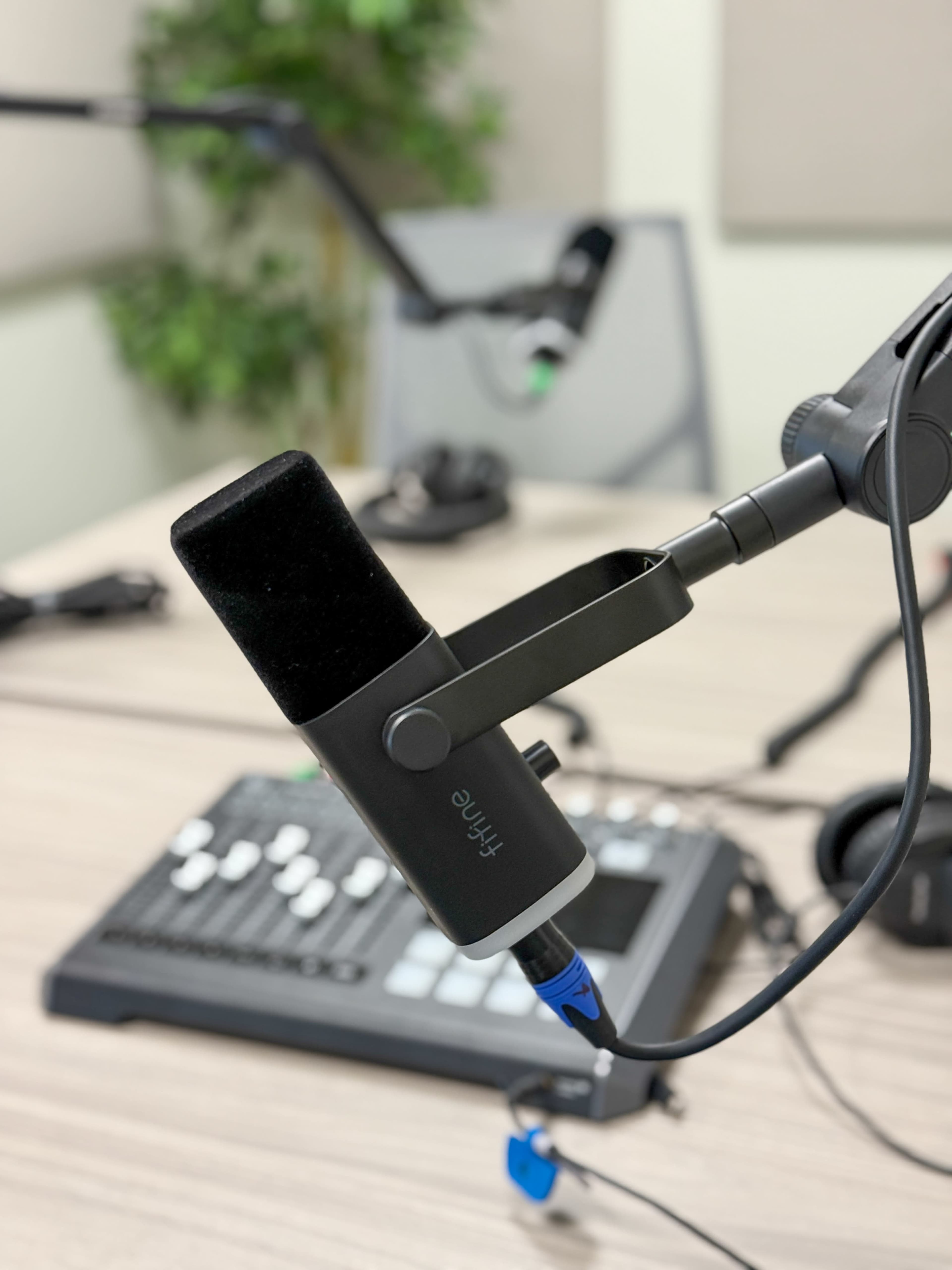 A microphone is mounted on an adjustable arm above a sound mixing console and headphones on a table in a recording studio.