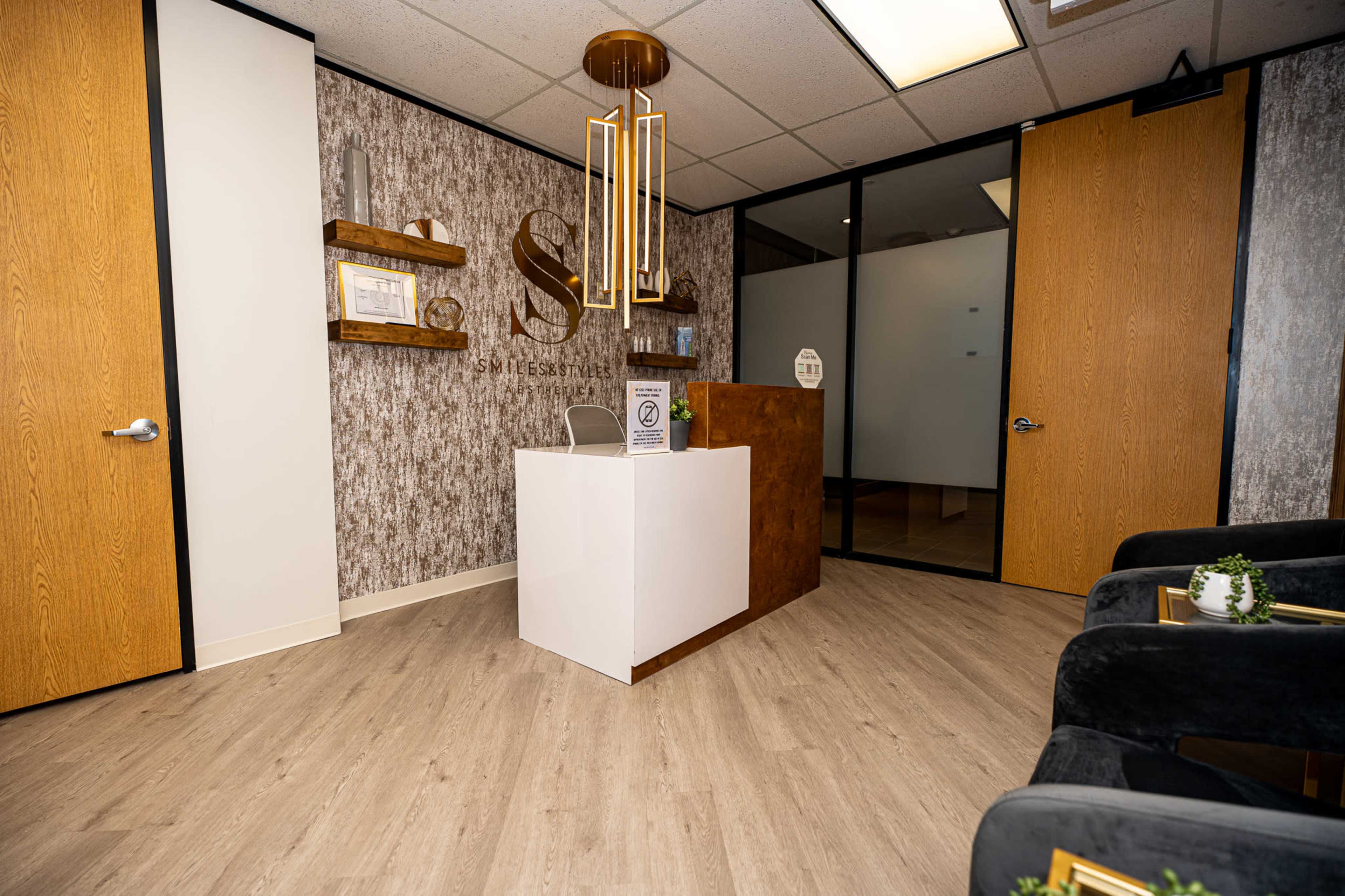 The image shows a modern reception area featuring a sleek front desk, decorative wall accents, and seating areas.