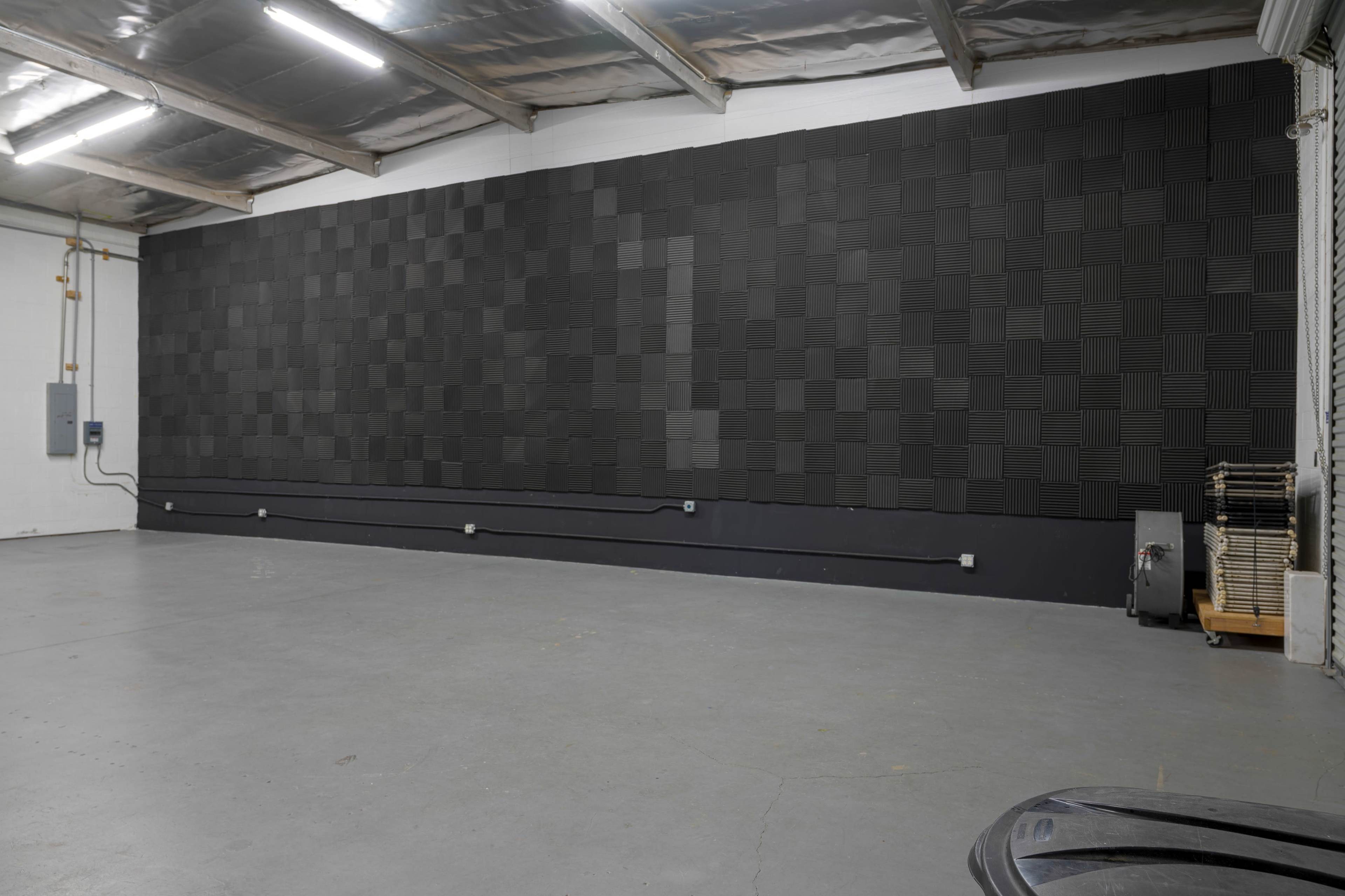 A large wall covered with black sound-absorbing panels in an empty industrial space.