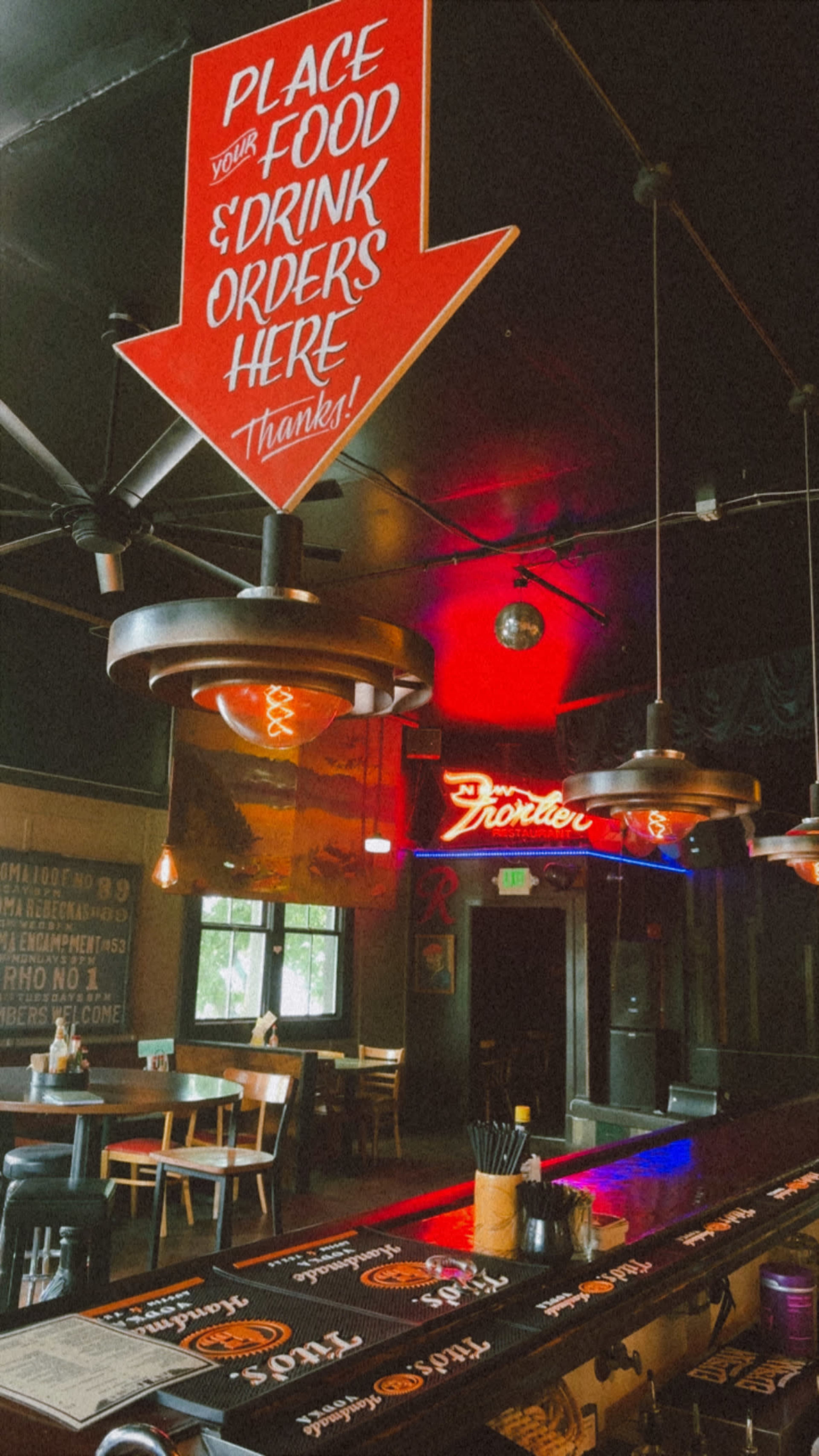 The image shows a dimly lit bar area with a red illuminated sign directing patrons to place their food and drink orders.