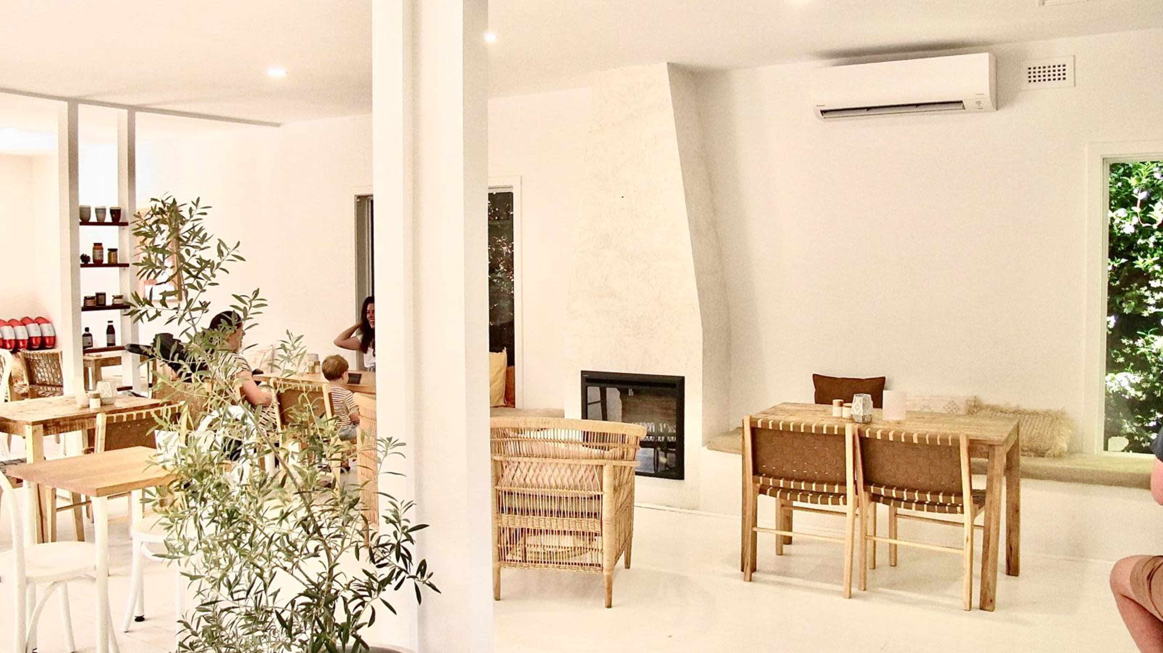 A bright, modern café interior with wooden tables, a fireplace, and leafy plants.