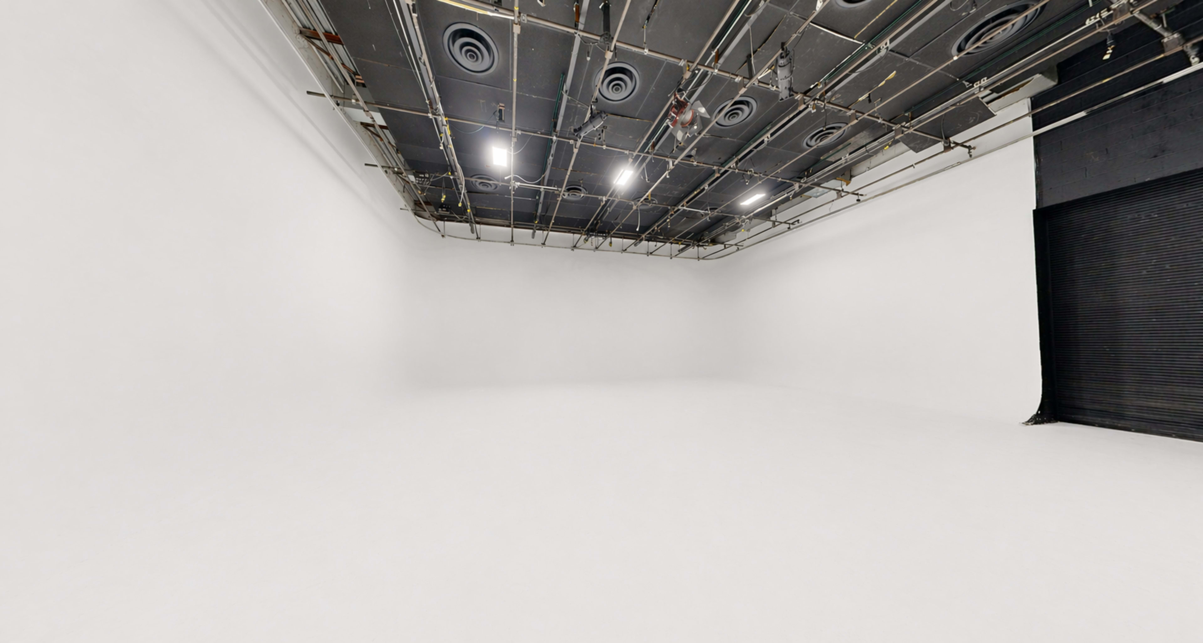 The image shows a spacious, empty studio with white walls and a seamless floor, illuminated by overhead lights.