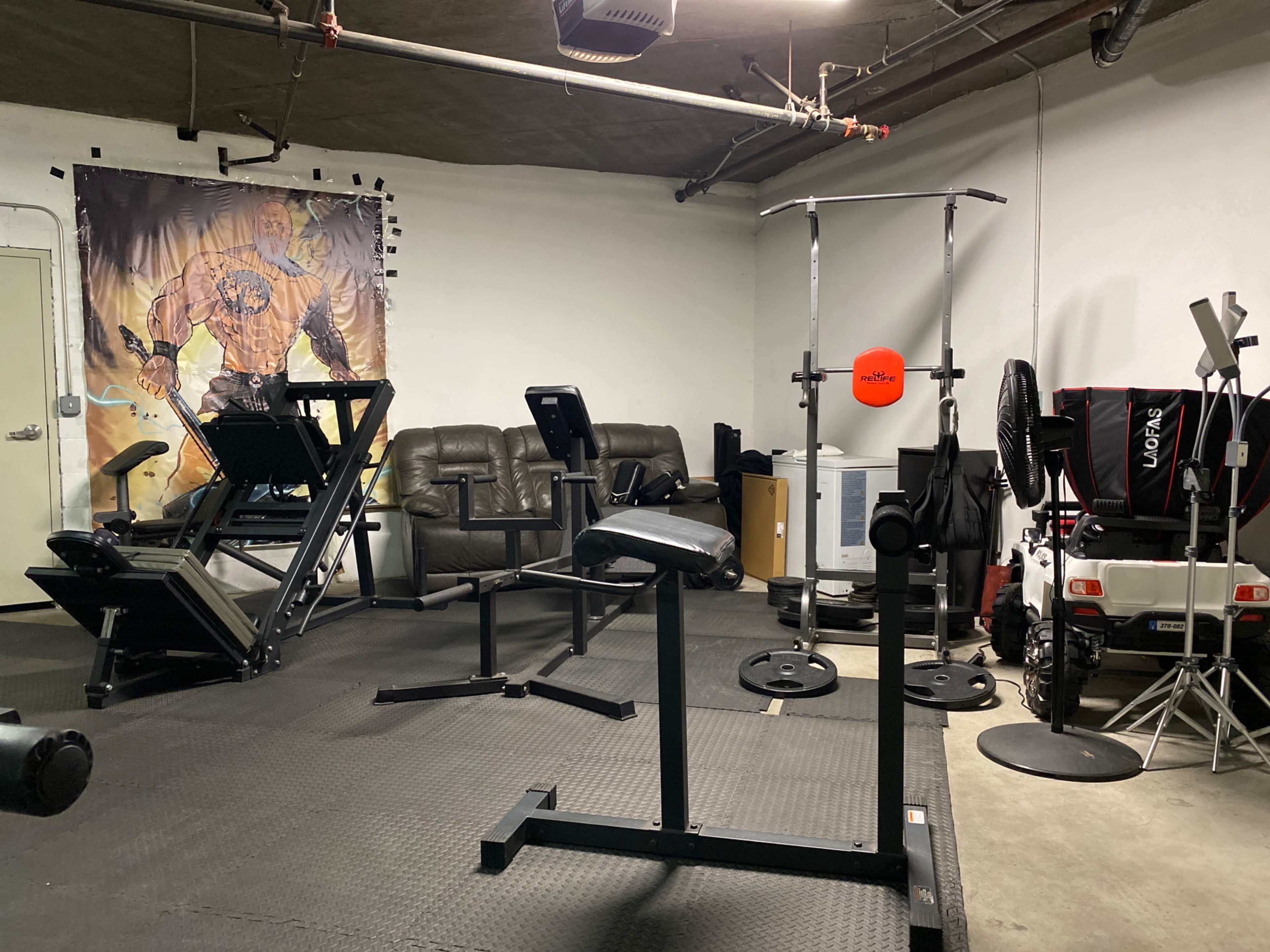 A gym space with various workout equipment, including a weight bench, a leg press machine, and a cable machine, against a backdrop of a graphic poster.