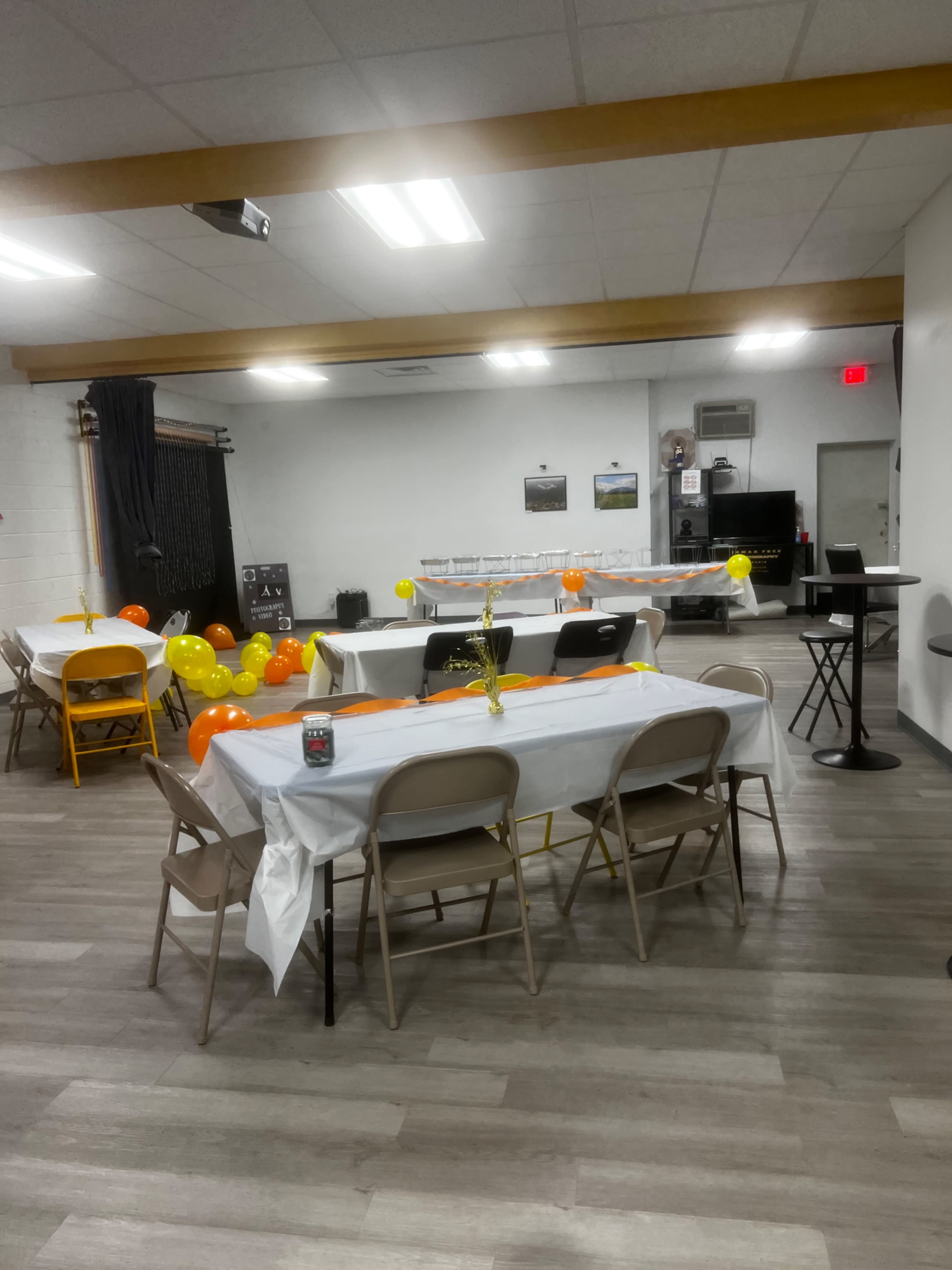 The room features several tables covered with white tablecloths and decorated with orange and yellow balloons.