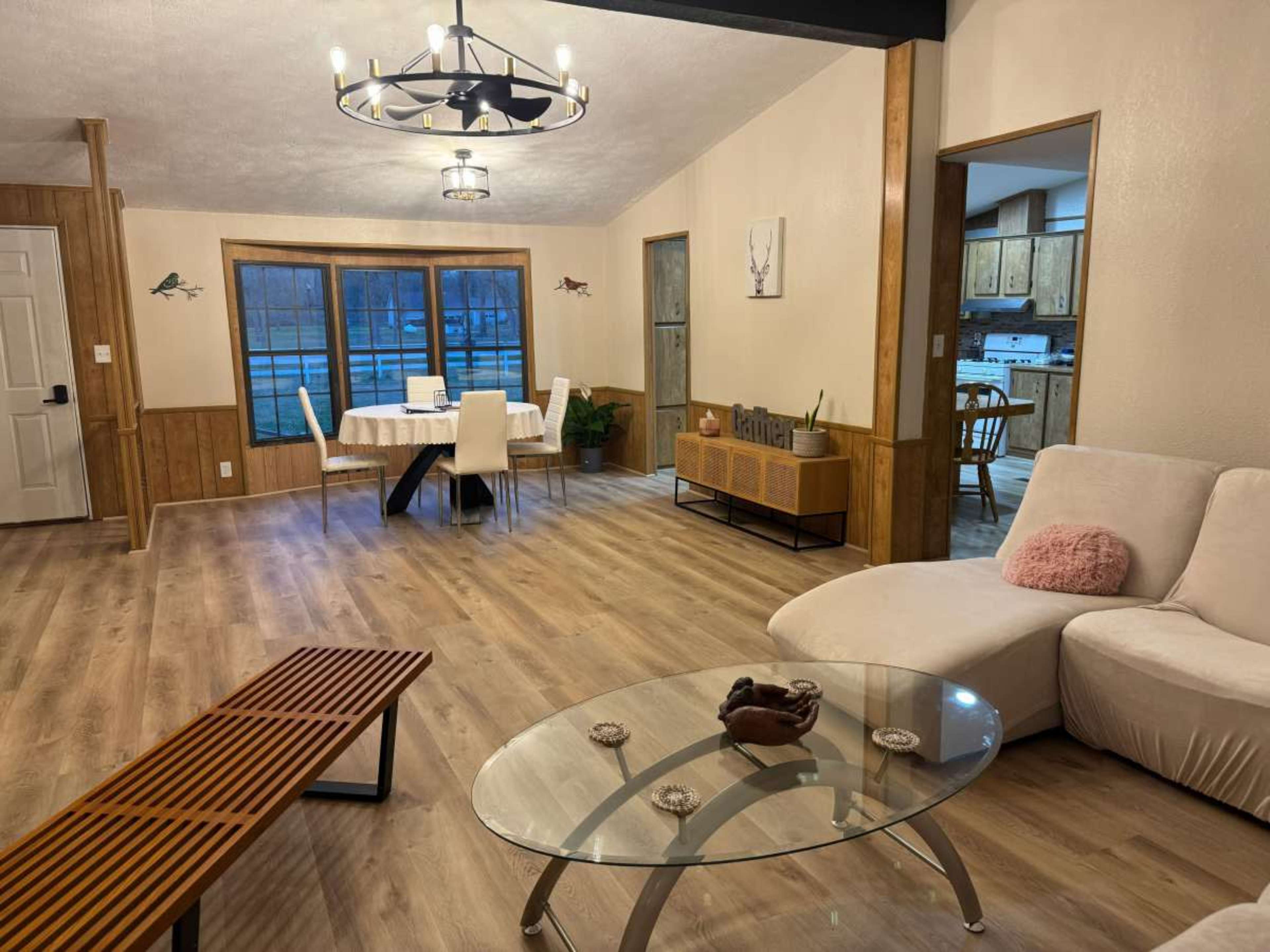 The image shows a modern interior space featuring a living area with a white sofa, a glass coffee table, and a dining area in the background with a table and chairs.
