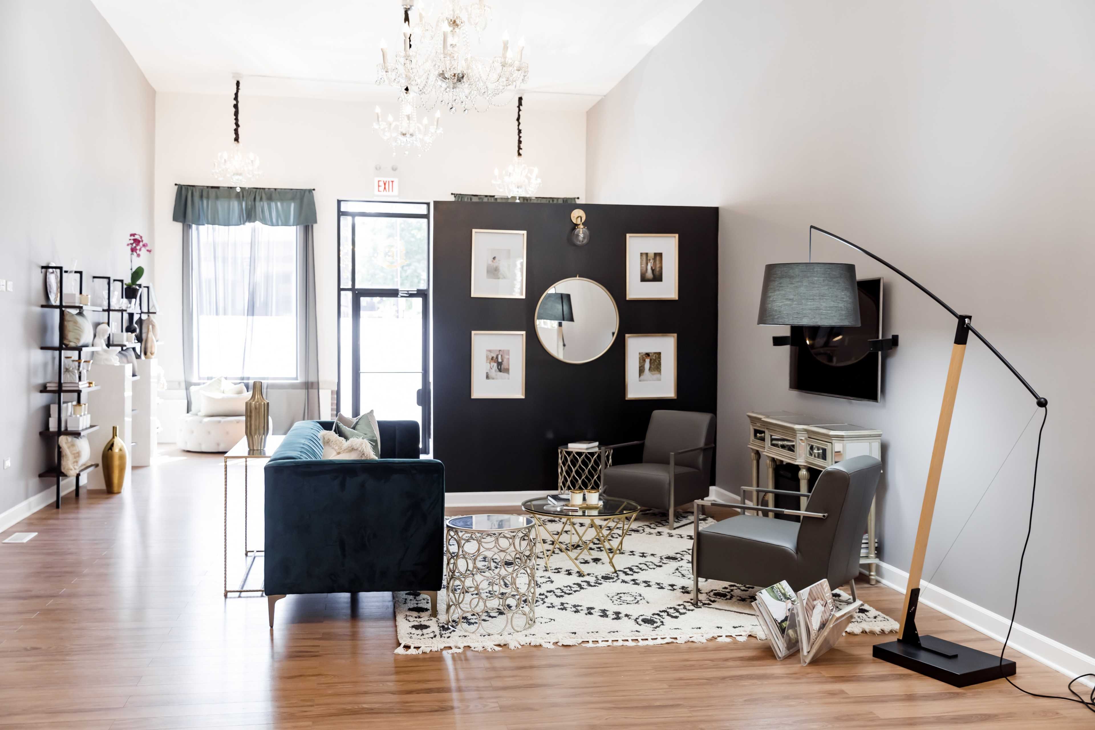 A modern living space with a teal sofa, two gray chairs, a round mirror on a black accent wall, and decorative elements including a coffee table and a floor lamp.