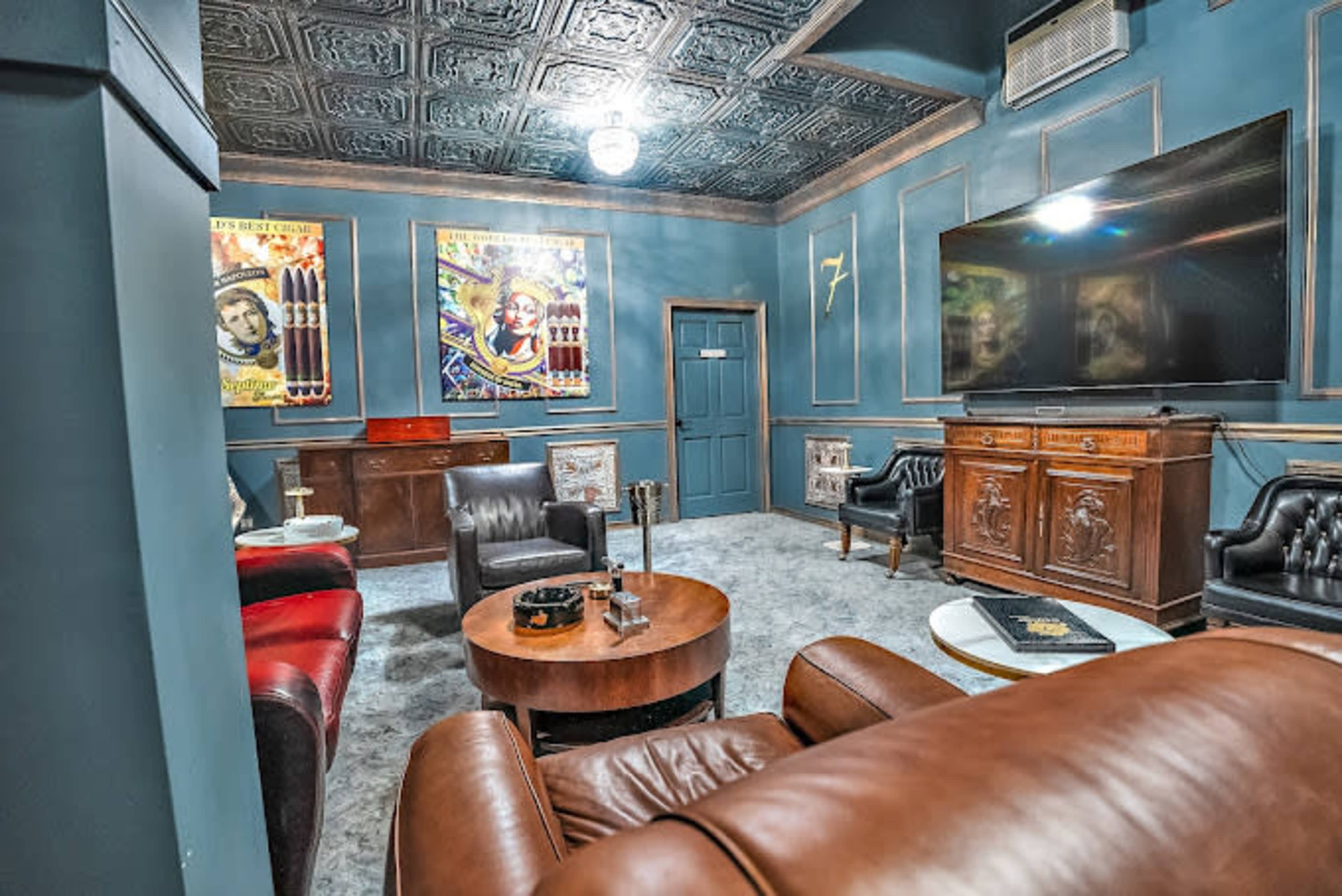 The room features dark blue walls, vintage artwork, leather seating, and a large television on an ornate cabinet.