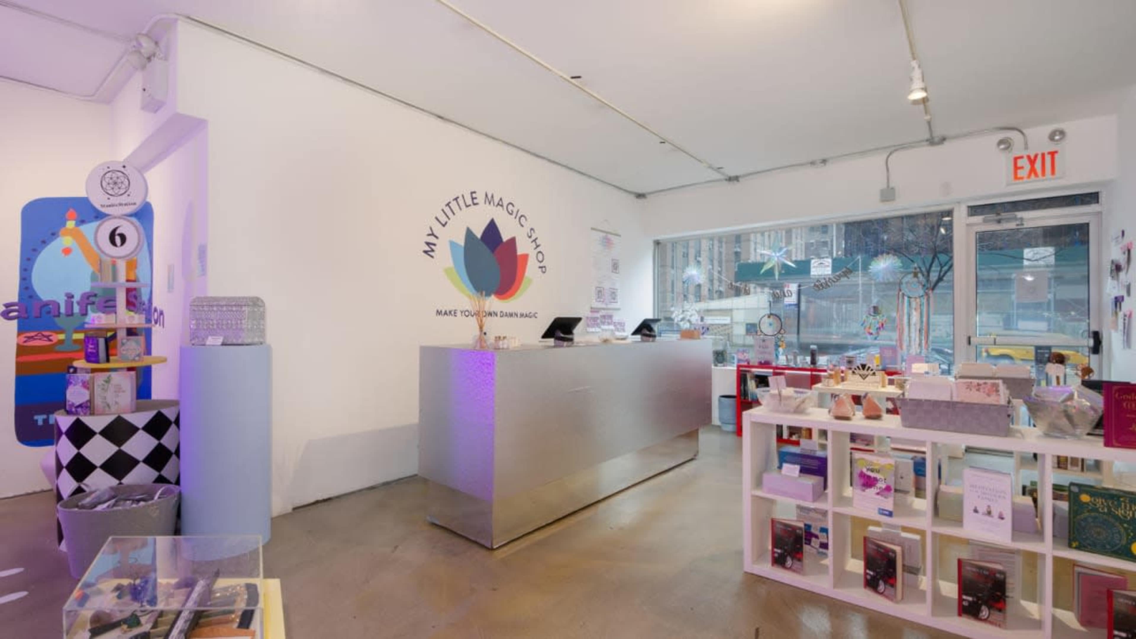 The image shows the interior of a shop named "My Little Magic Shop," featuring a sleek silver counter and various colorful merchandise displays.
