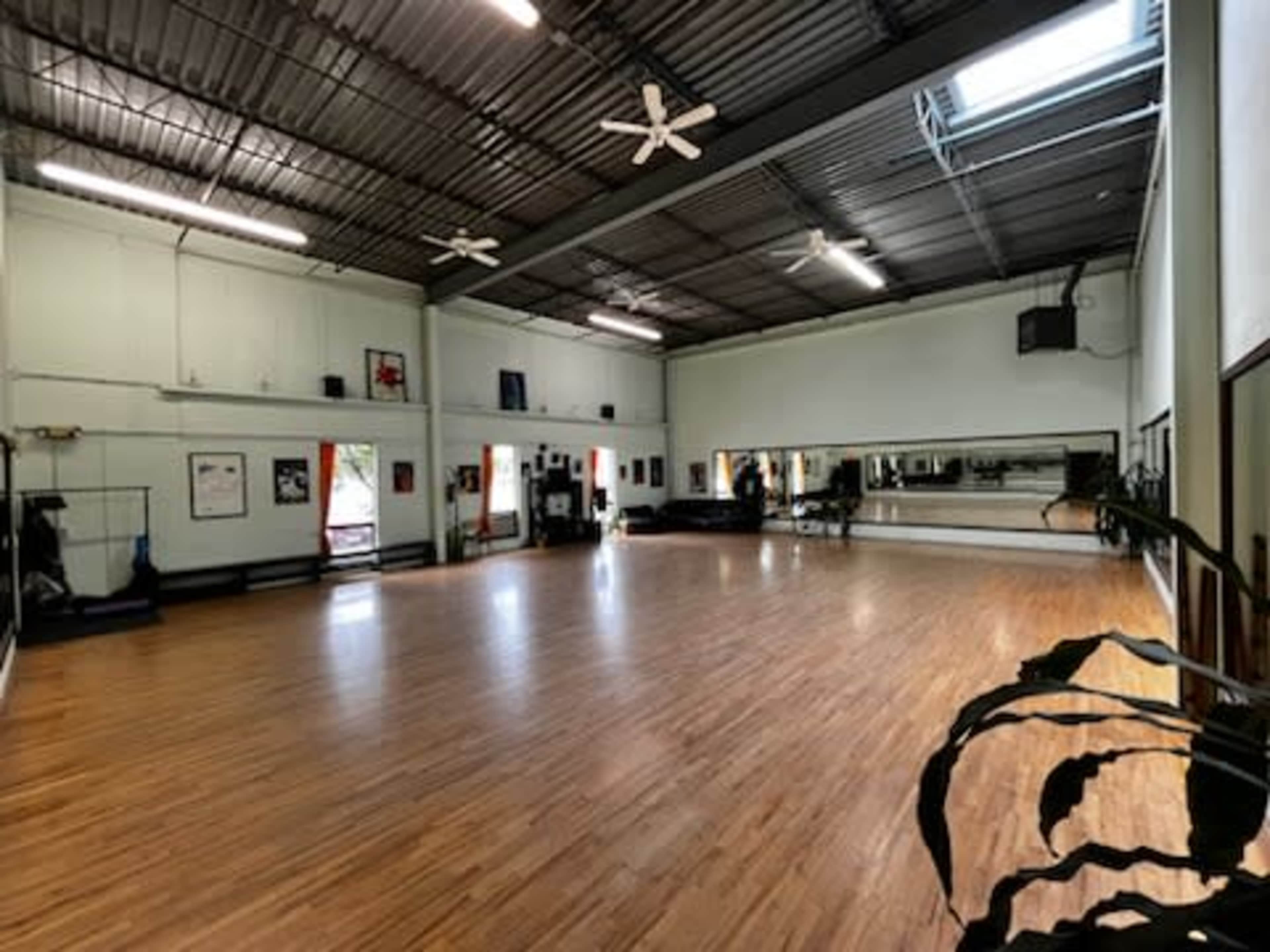 A spacious dance studio with wooden flooring, large mirrors, and bright overhead lights.