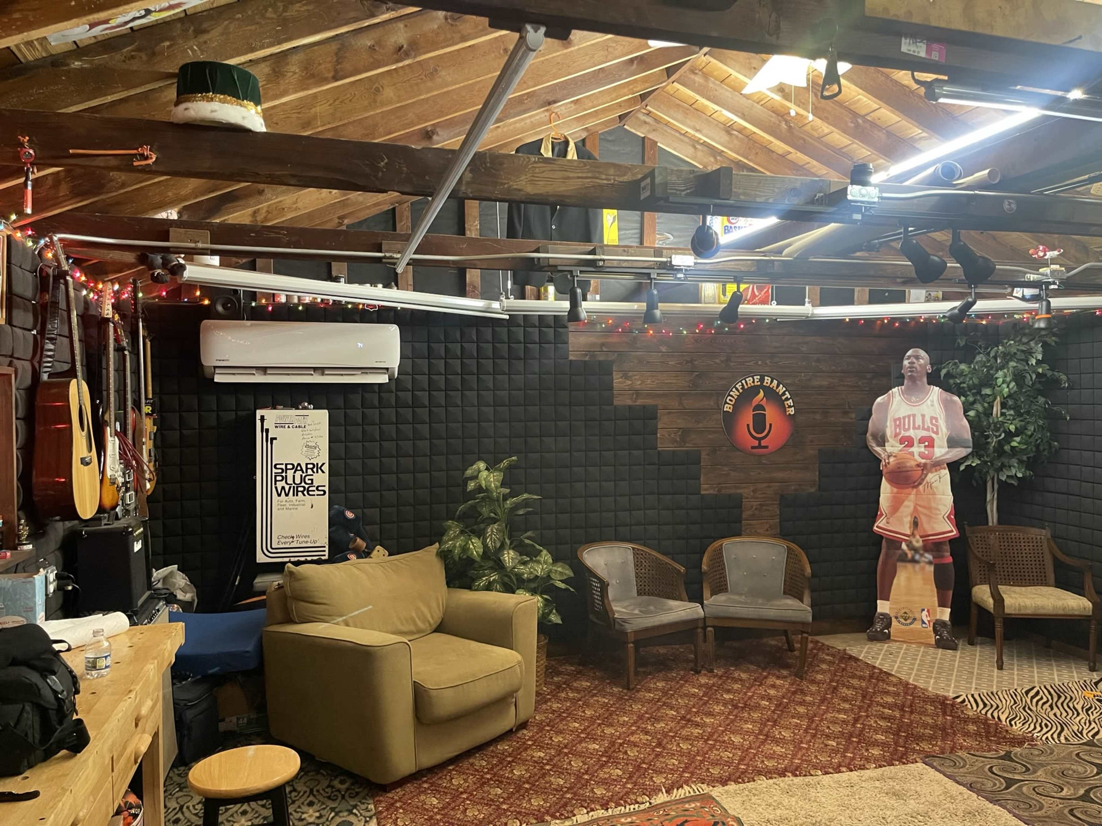 A cozy indoor space with wooden beams and walls, featuring a seating area with a sofa and chairs, decorated with string lights and music instruments.