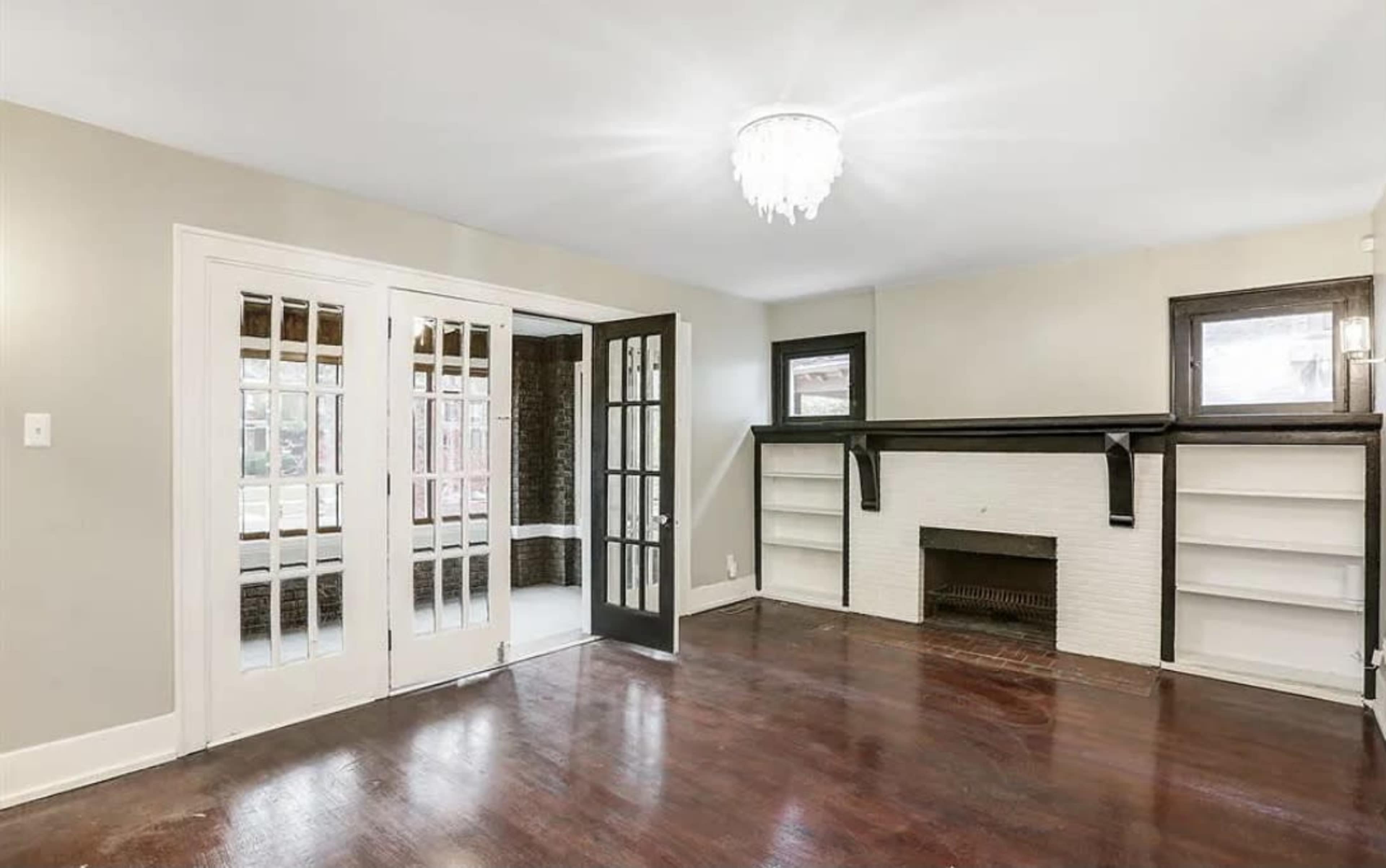 A spacious room with dark wooden floors, a fireplace, built-in shelves, and large glass doors leading to another area.