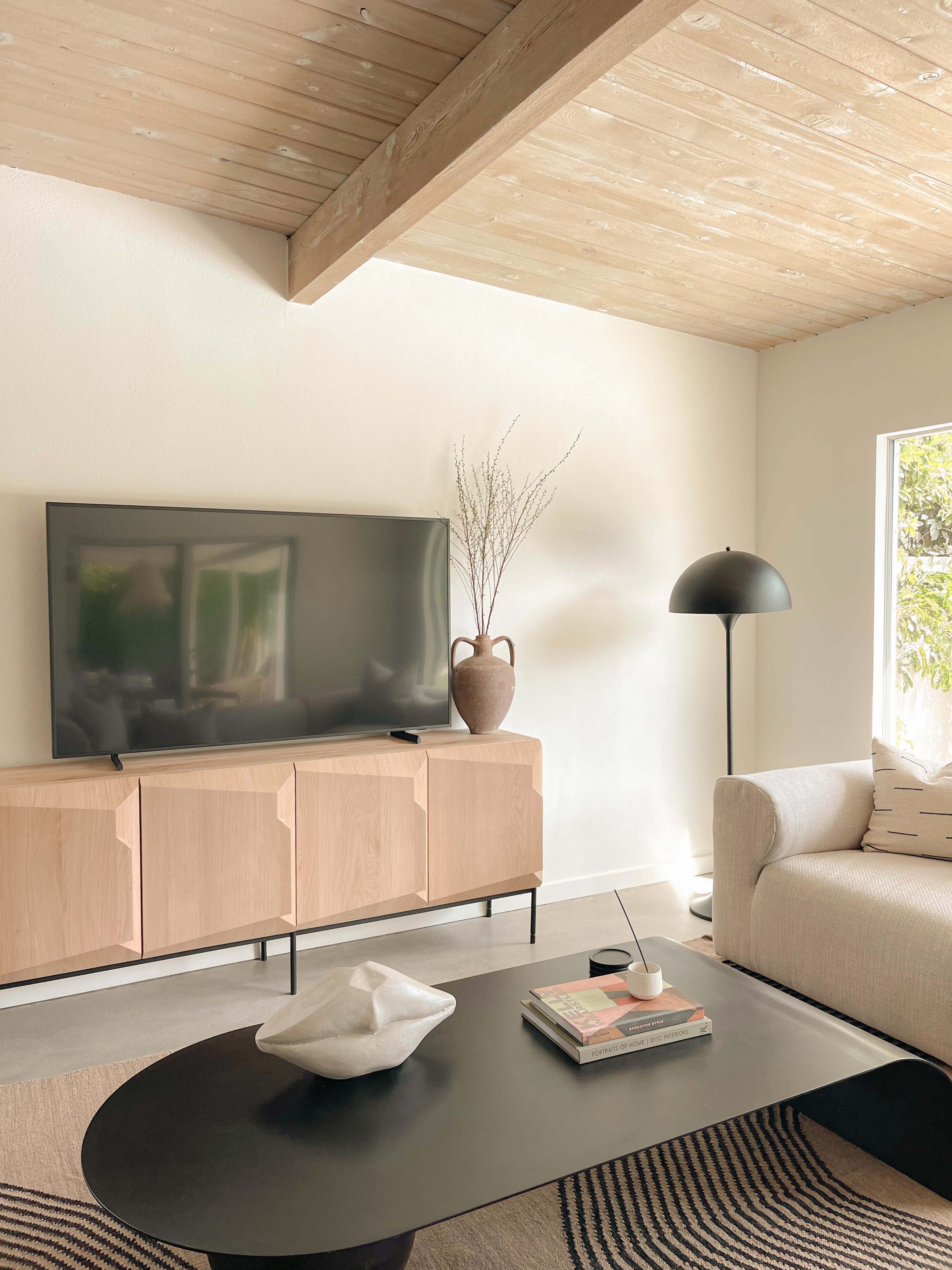 A modern living room features a television mounted on the wall above a light wood sideboard, with a coffee table, a floor lamp, and a cozy sofa.