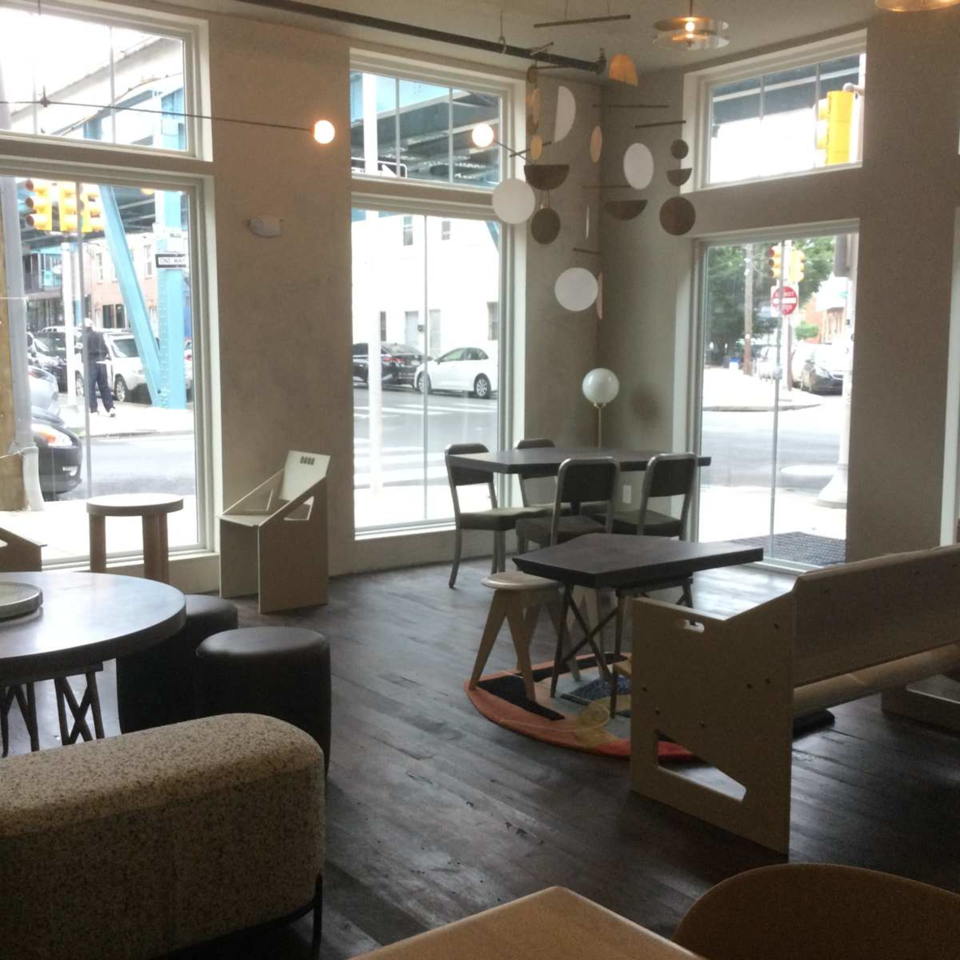 The image shows a modern café interior with various seating arrangements and large windows allowing natural light to enter.