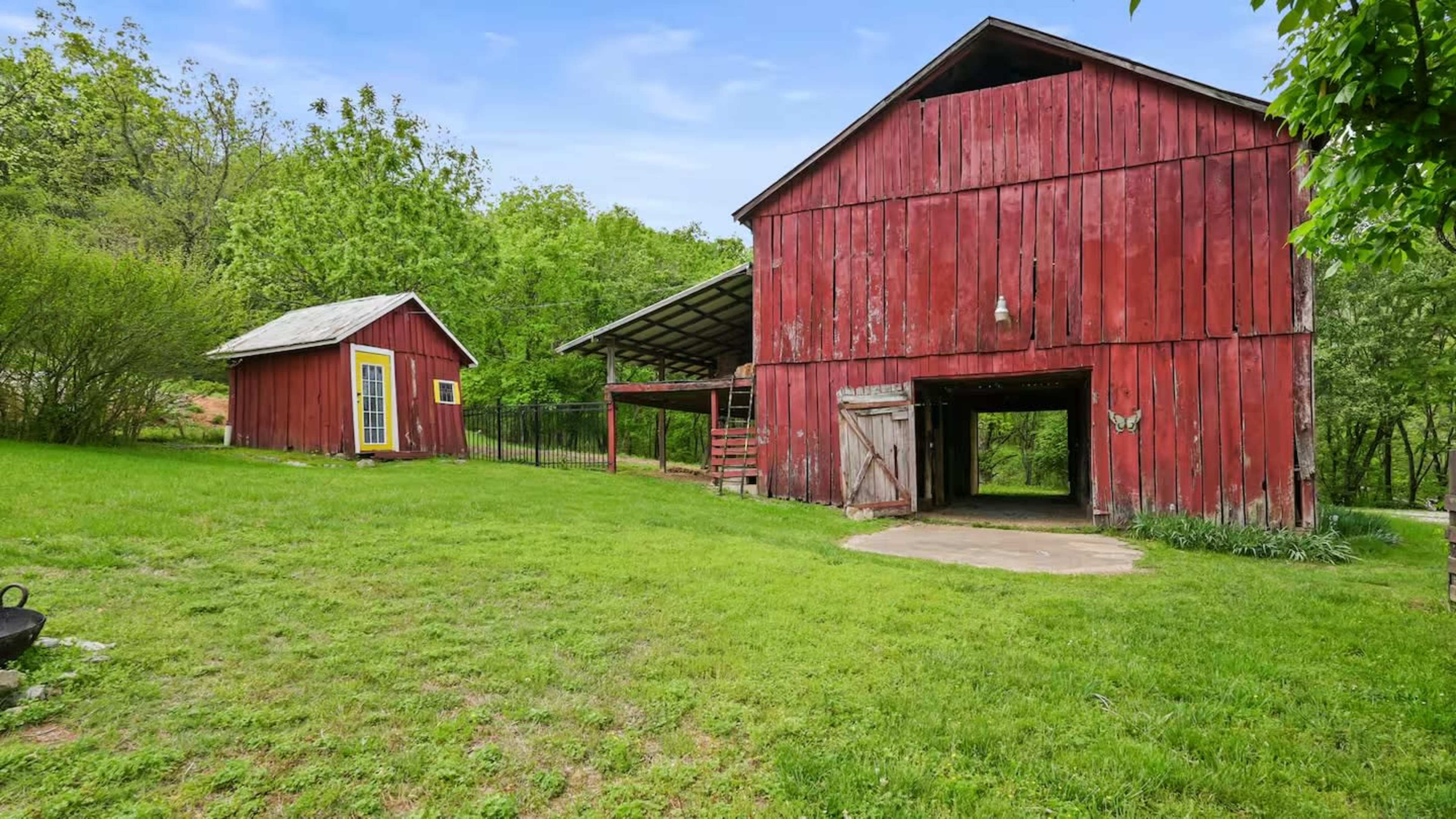 The image shows a red barn and a small shed surrounded by green grass and trees.
