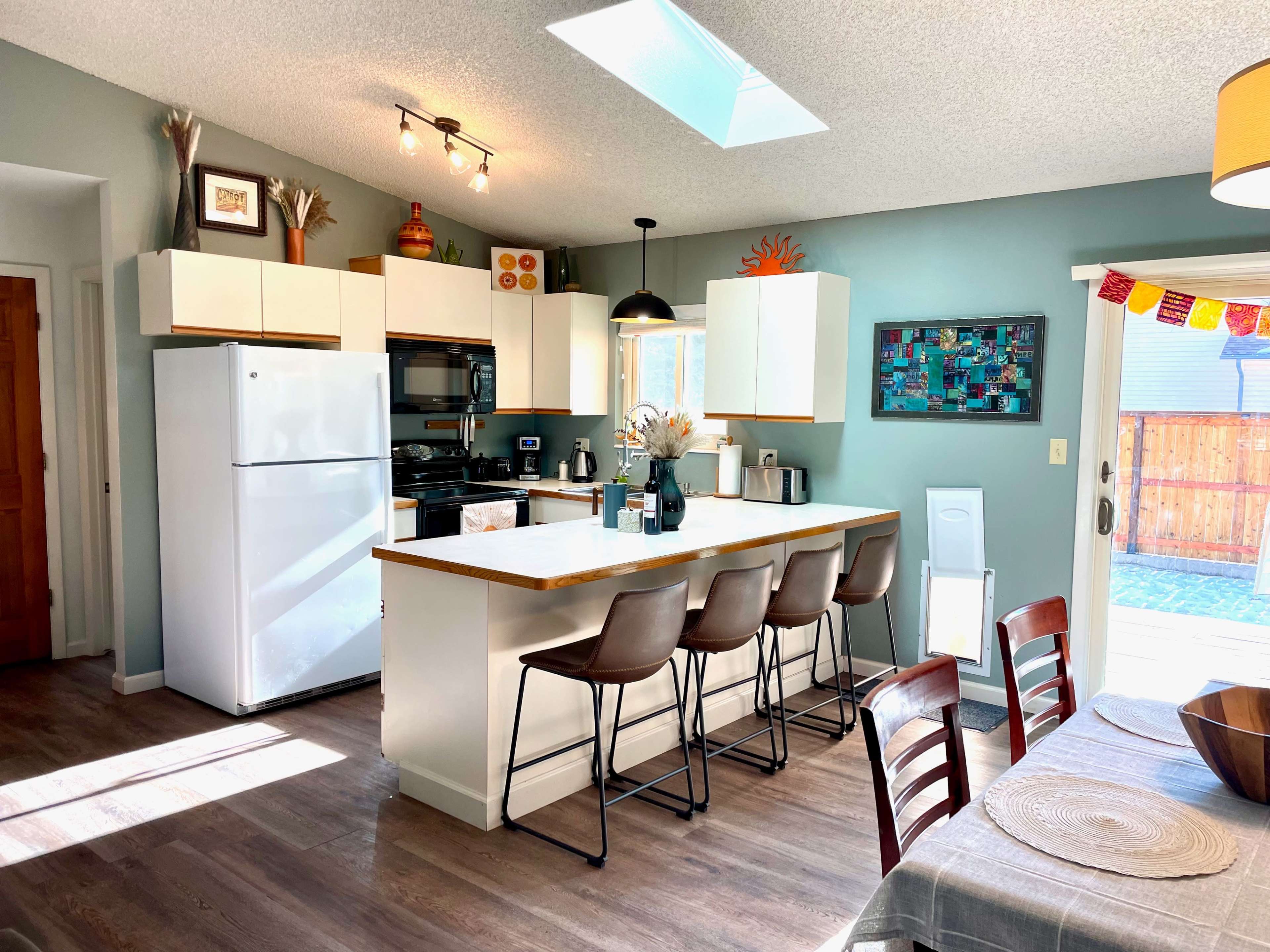 A modern kitchen features white cabinetry, stainless steel appliances, and a countertop with bar seating, illuminated by natural light through a skylight.