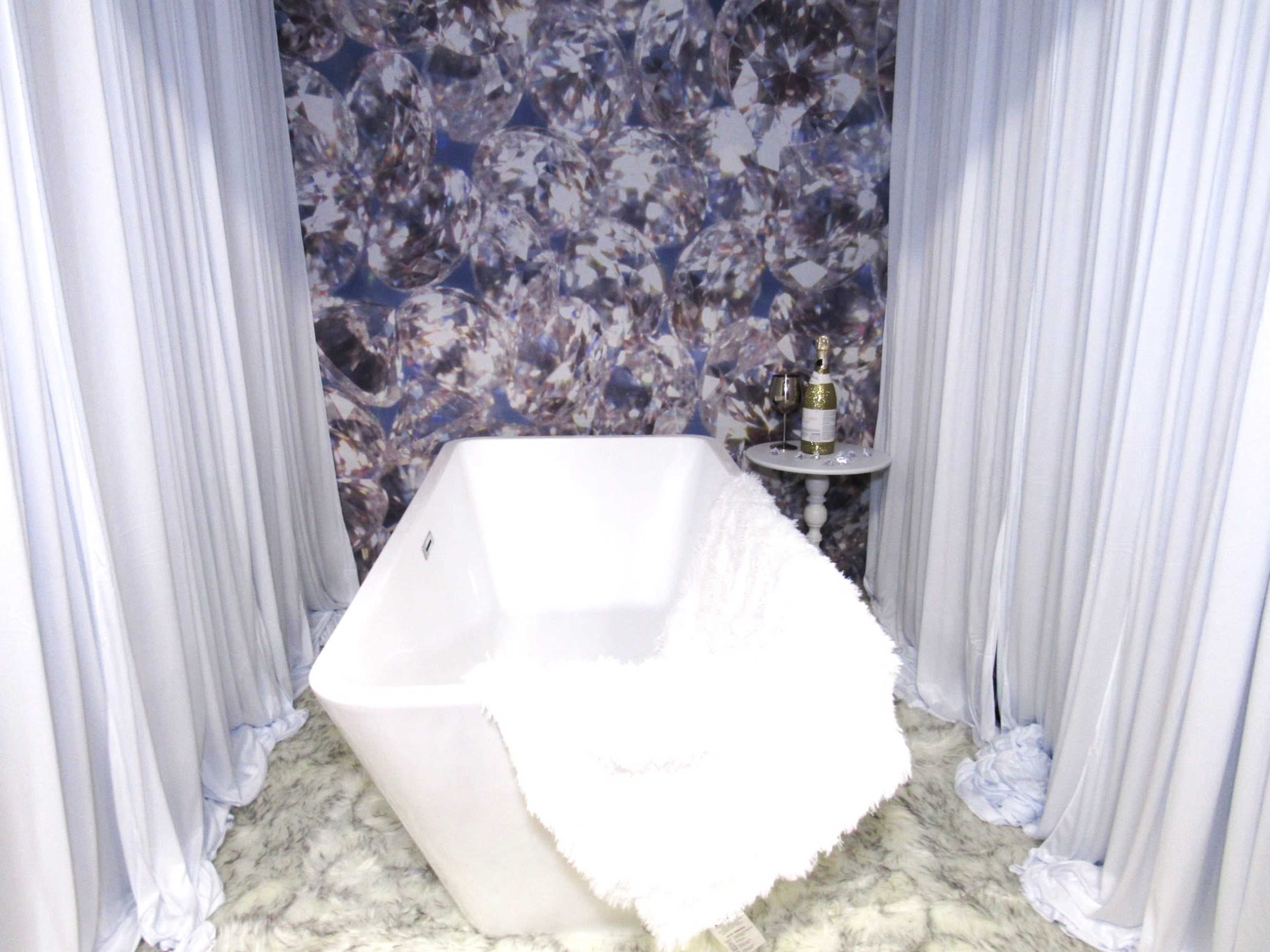 A modern bathroom features a white freestanding bathtub surrounded by sheer curtains and a plush rug.