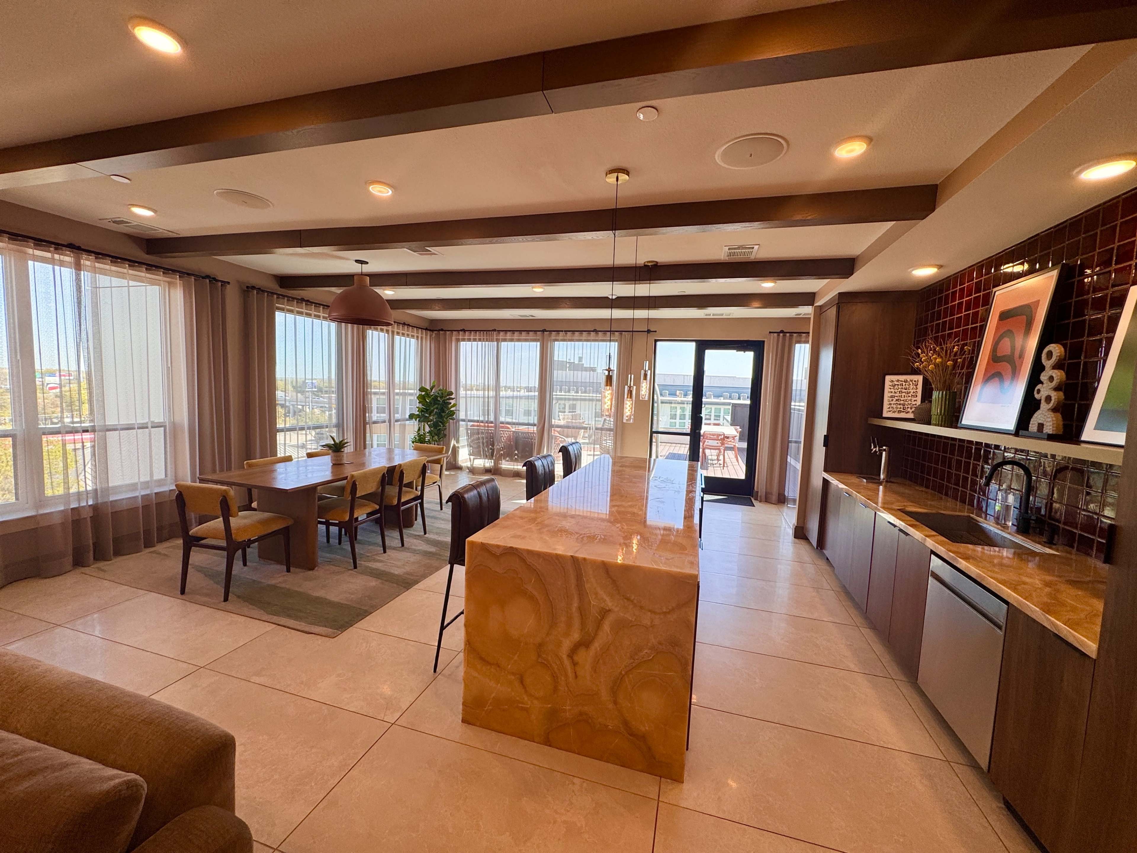 A spacious modern dining and kitchen area features large windows, a long dining table, and a marble countertop.