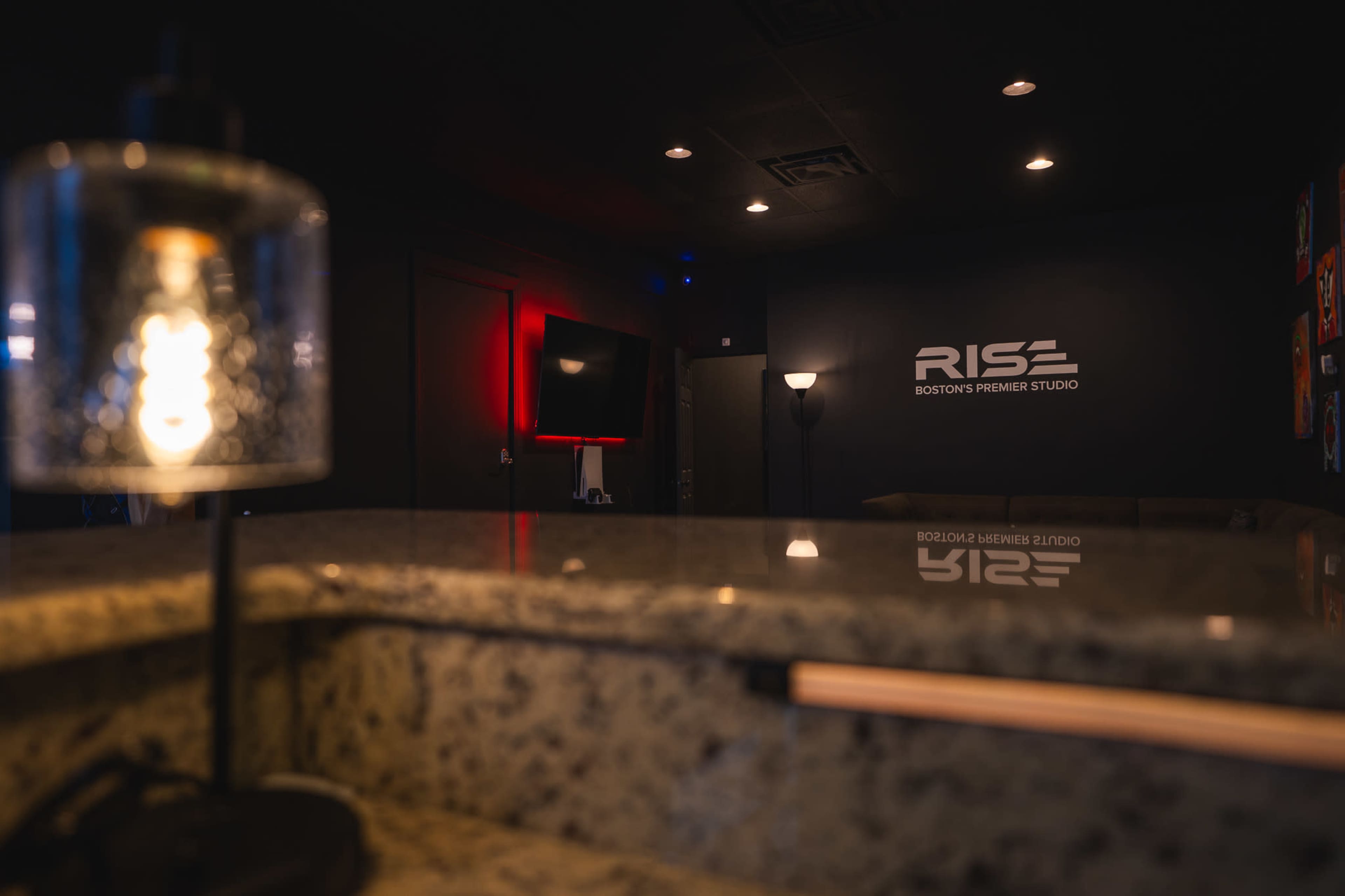 The image shows a dimly lit interior of a studio with the name "RISE" displayed on the wall, and a countertop in the foreground.