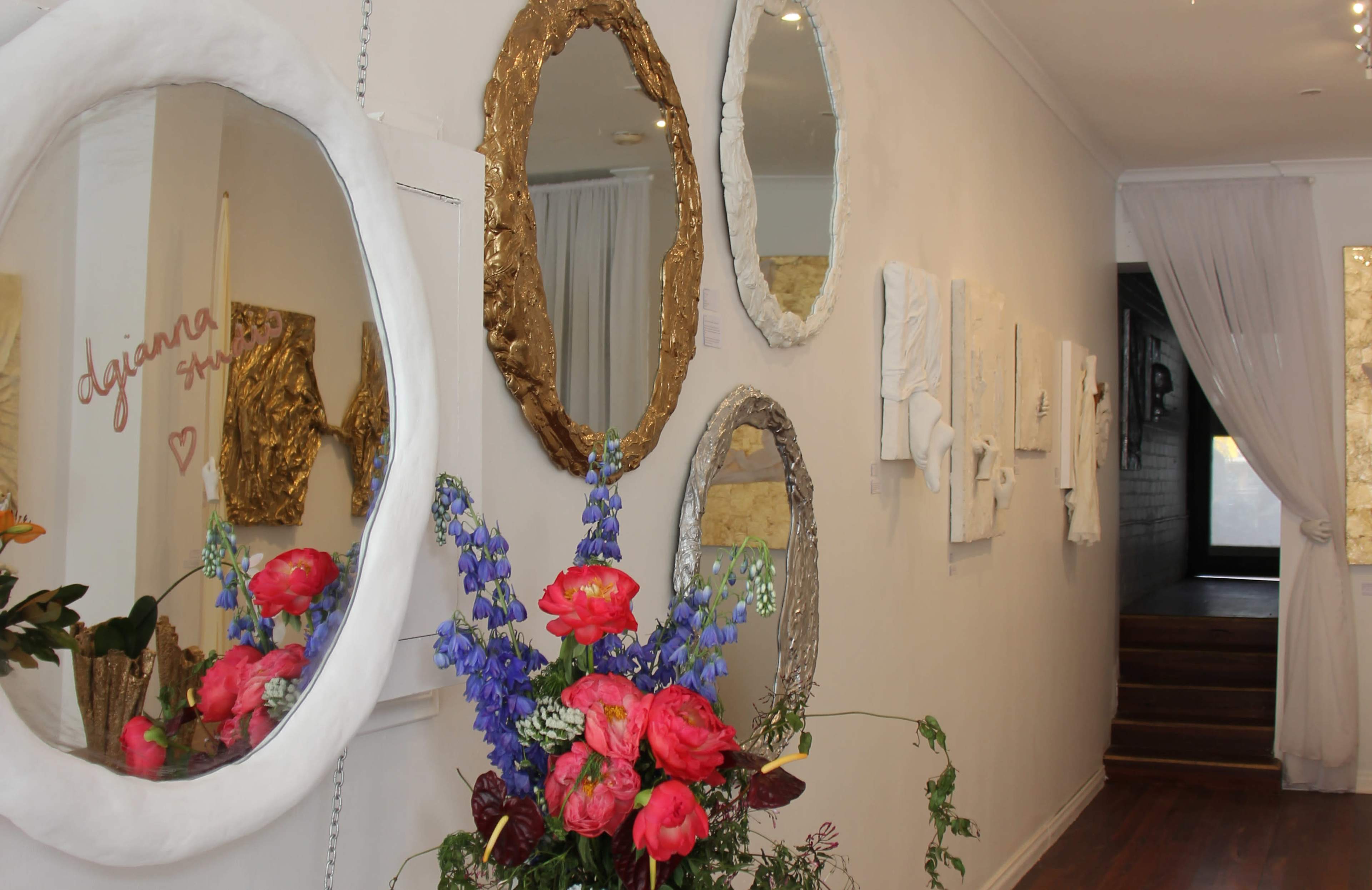 The image shows a hallway adorned with decorative mirrors and artworks, alongside a bouquet of colorful flowers placed in front of the mirrors.