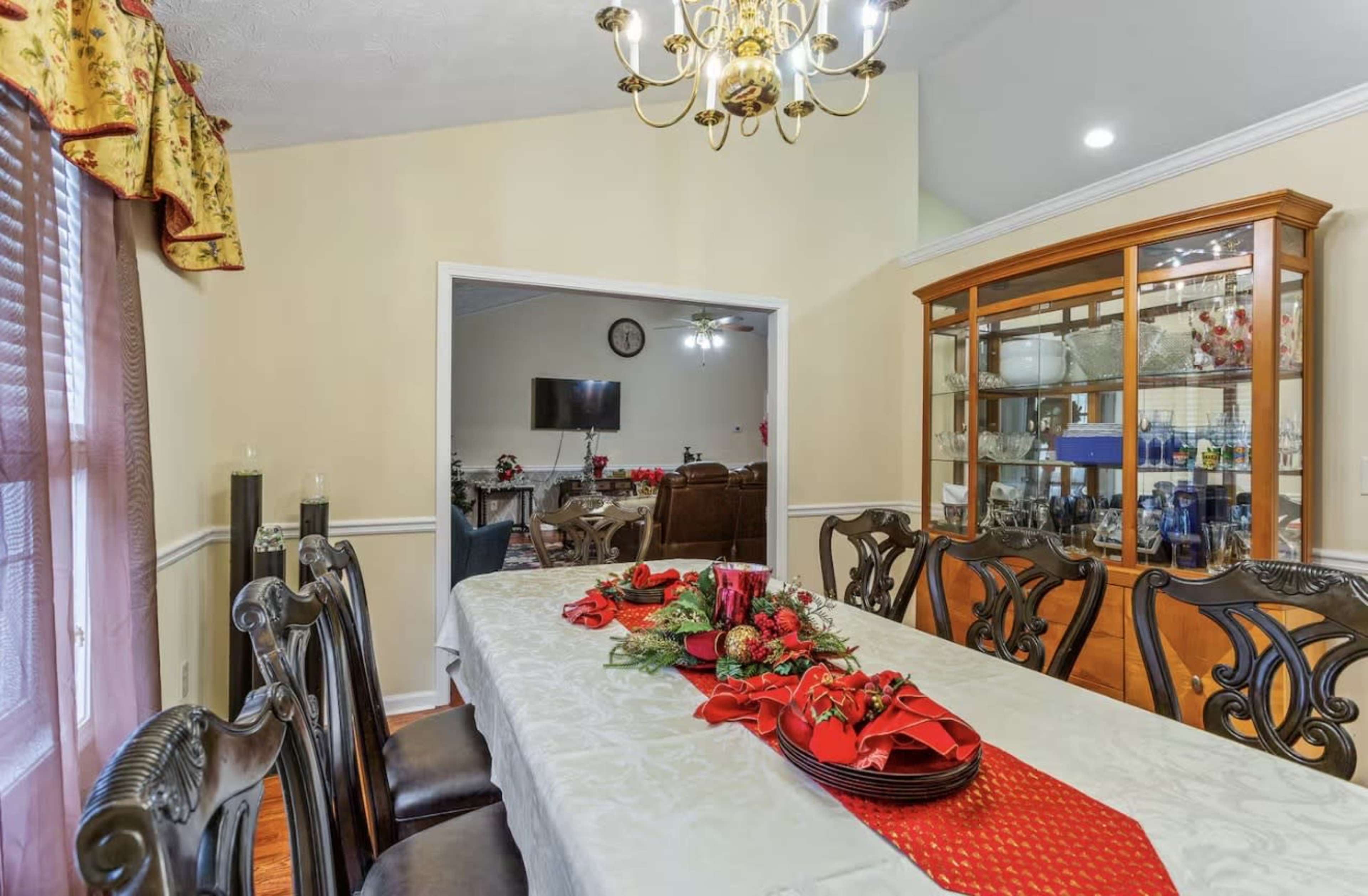 A neatly set dining table with a red and white floral centerpiece is surrounded by dark wooden chairs in a well-lit dining room.