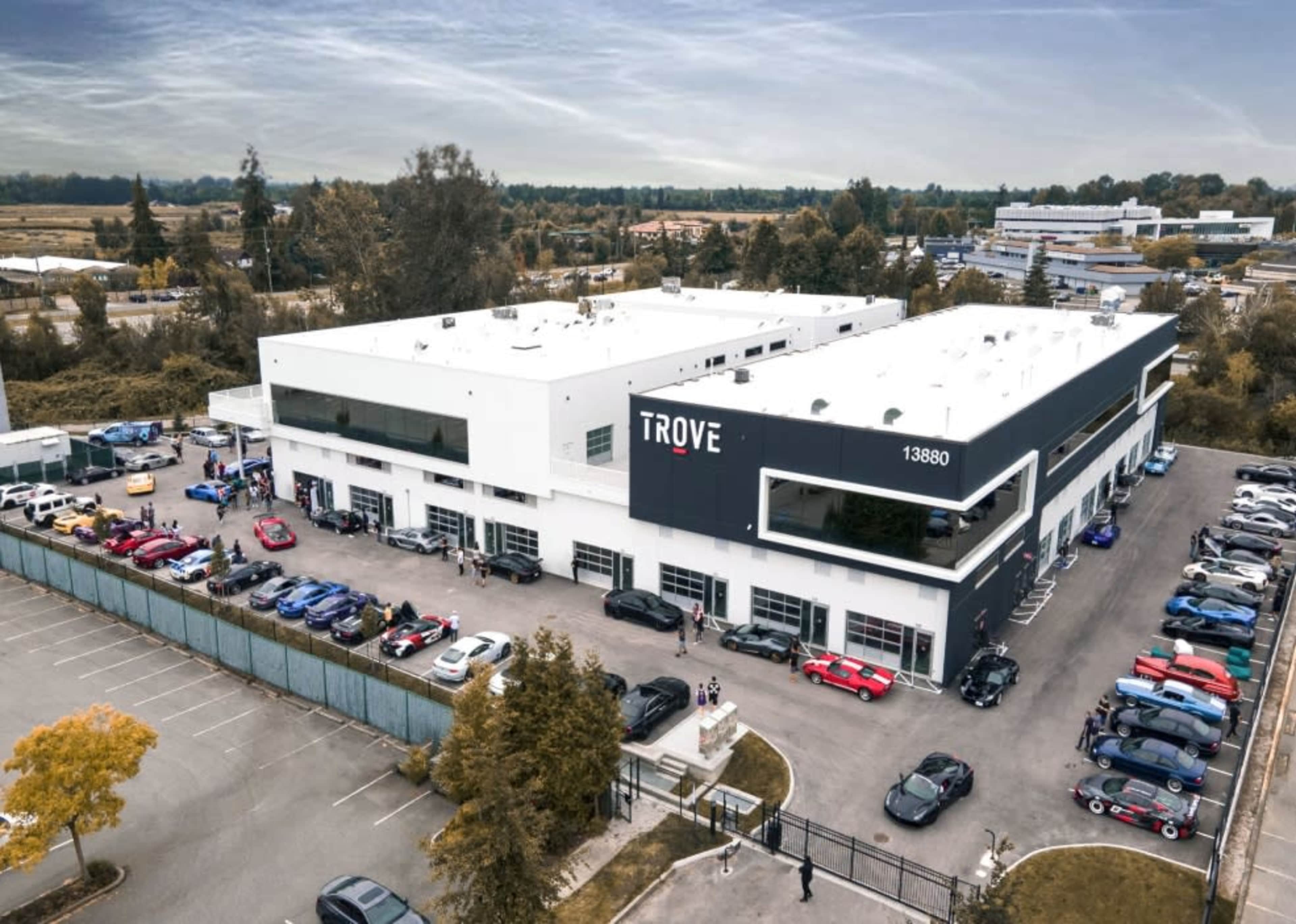A large industrial building named "TROVE" is surrounded by several parked cars in a lot, with additional buildings visible in the background.