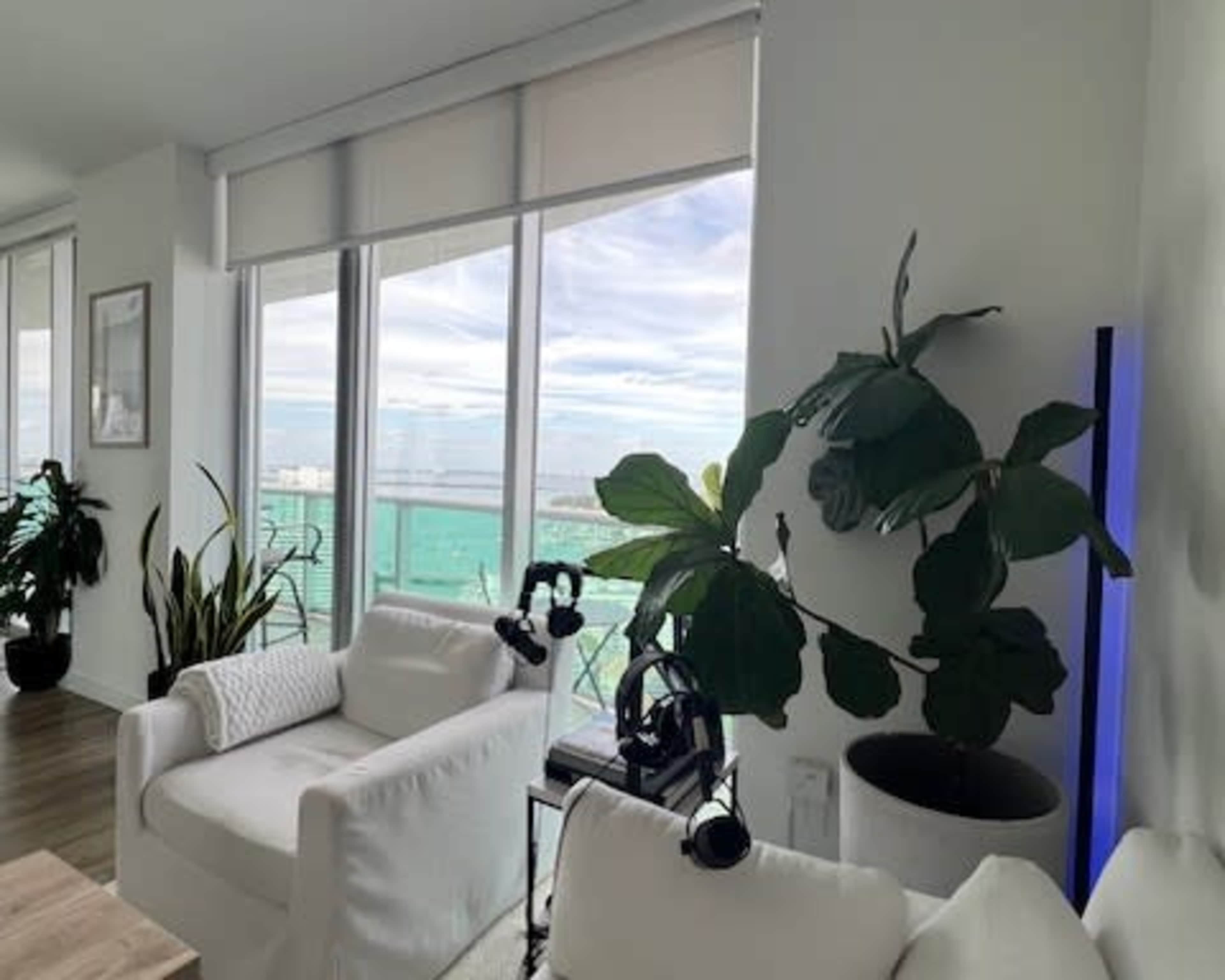 A cozy interior features a white couch and a potted plant near large windows with a view of the ocean.