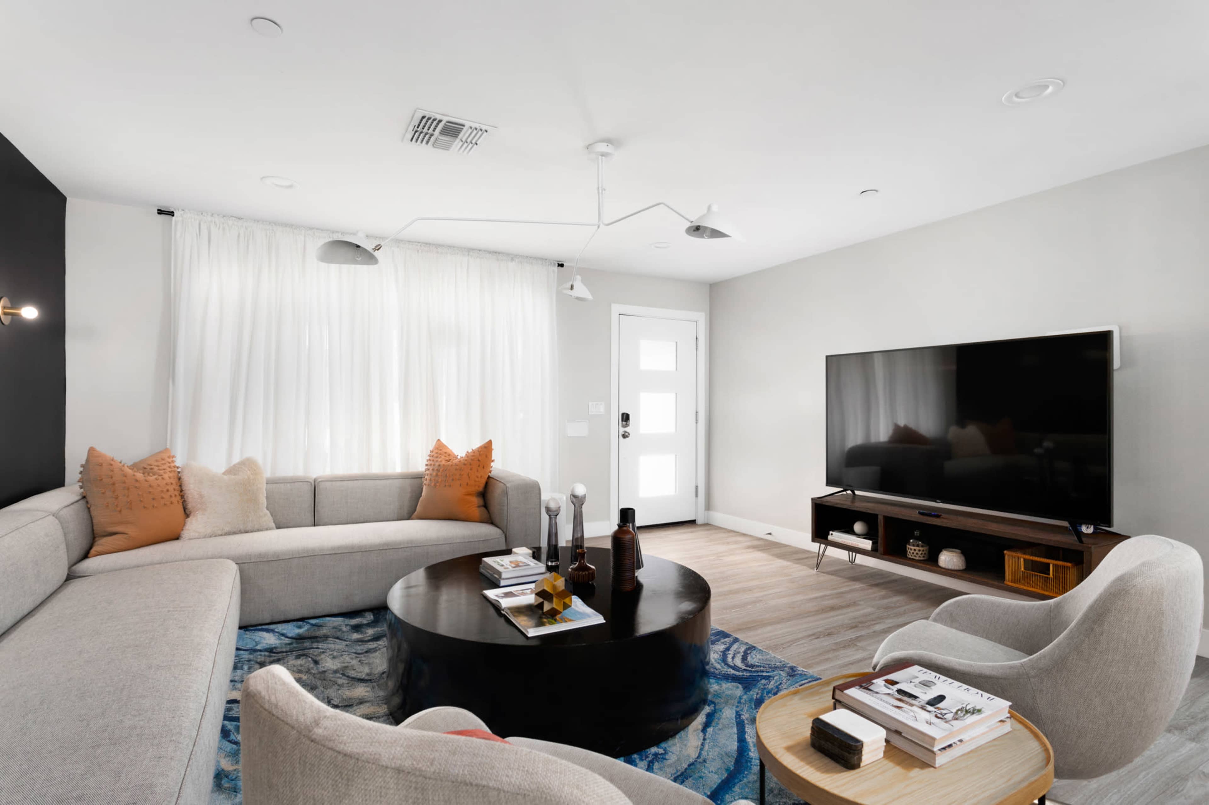 A modern living room featuring a gray sectional sofa, a round black coffee table, a large television, and a combination of light and dark decor elements.