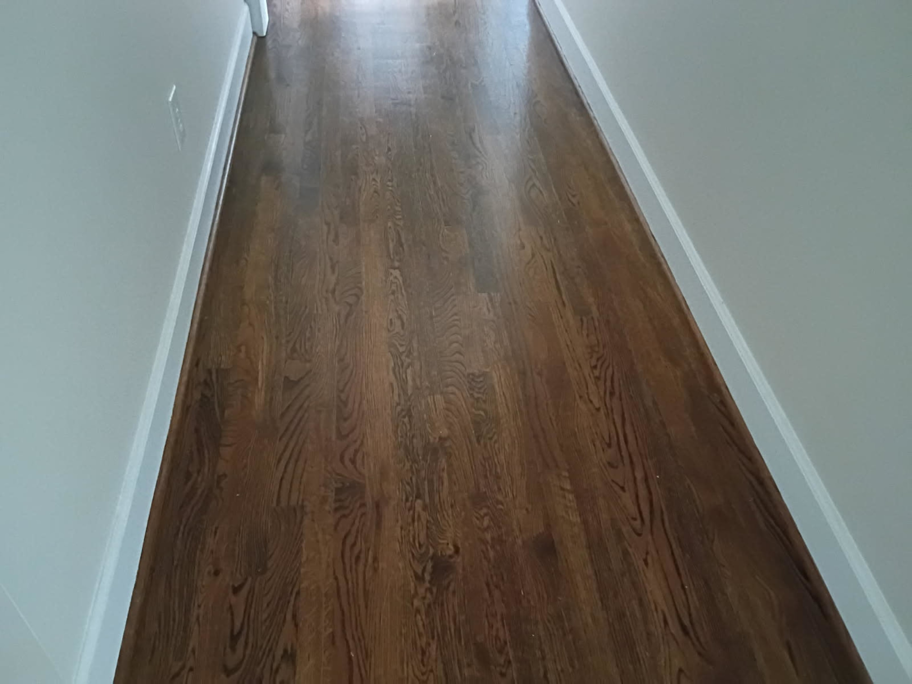 The image shows a long wood-floored hallway with white walls on either side.