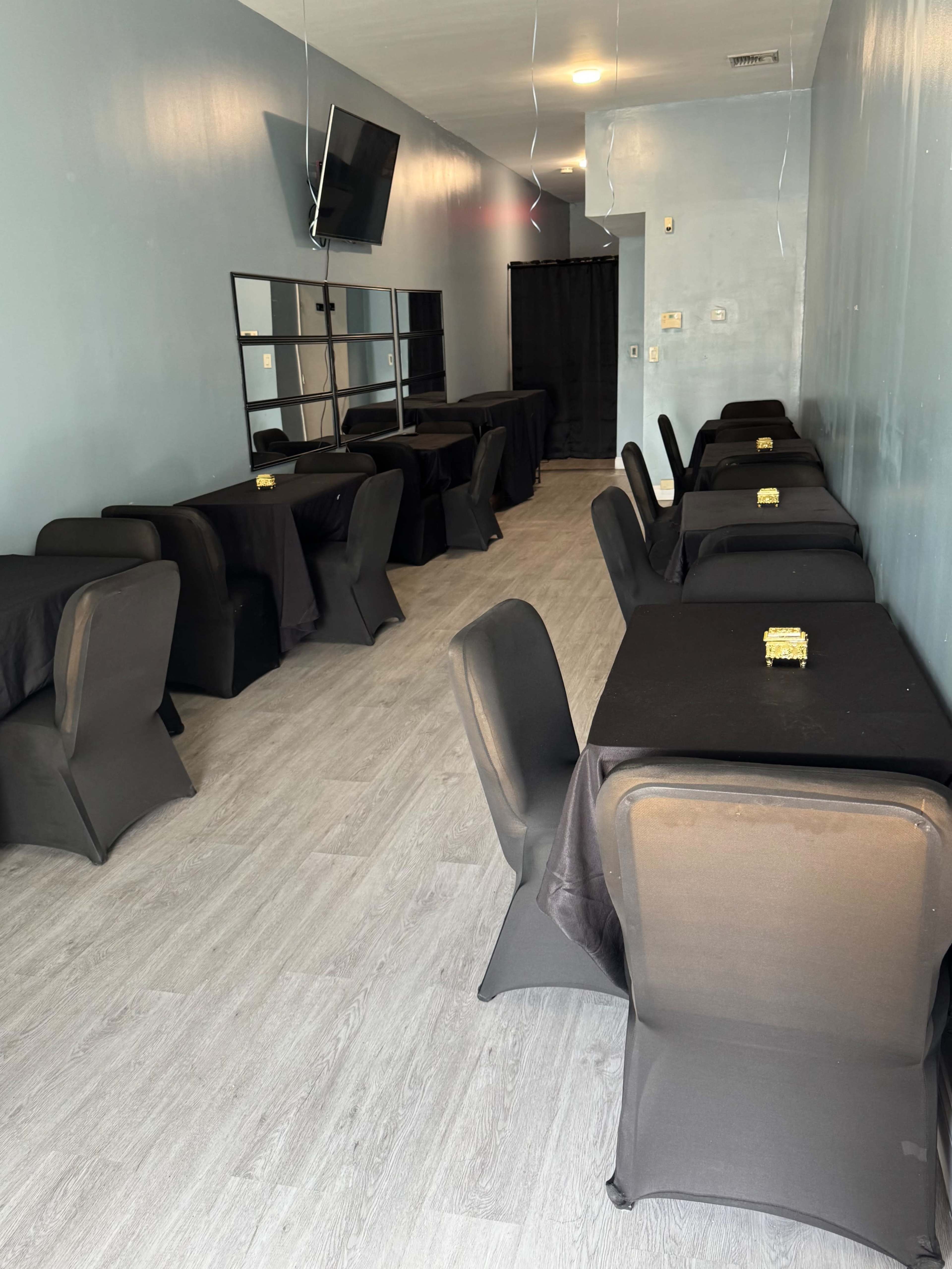 The image shows a spacious room with several covered tables arranged in rows, featuring black tablecloths and minimal decoration.