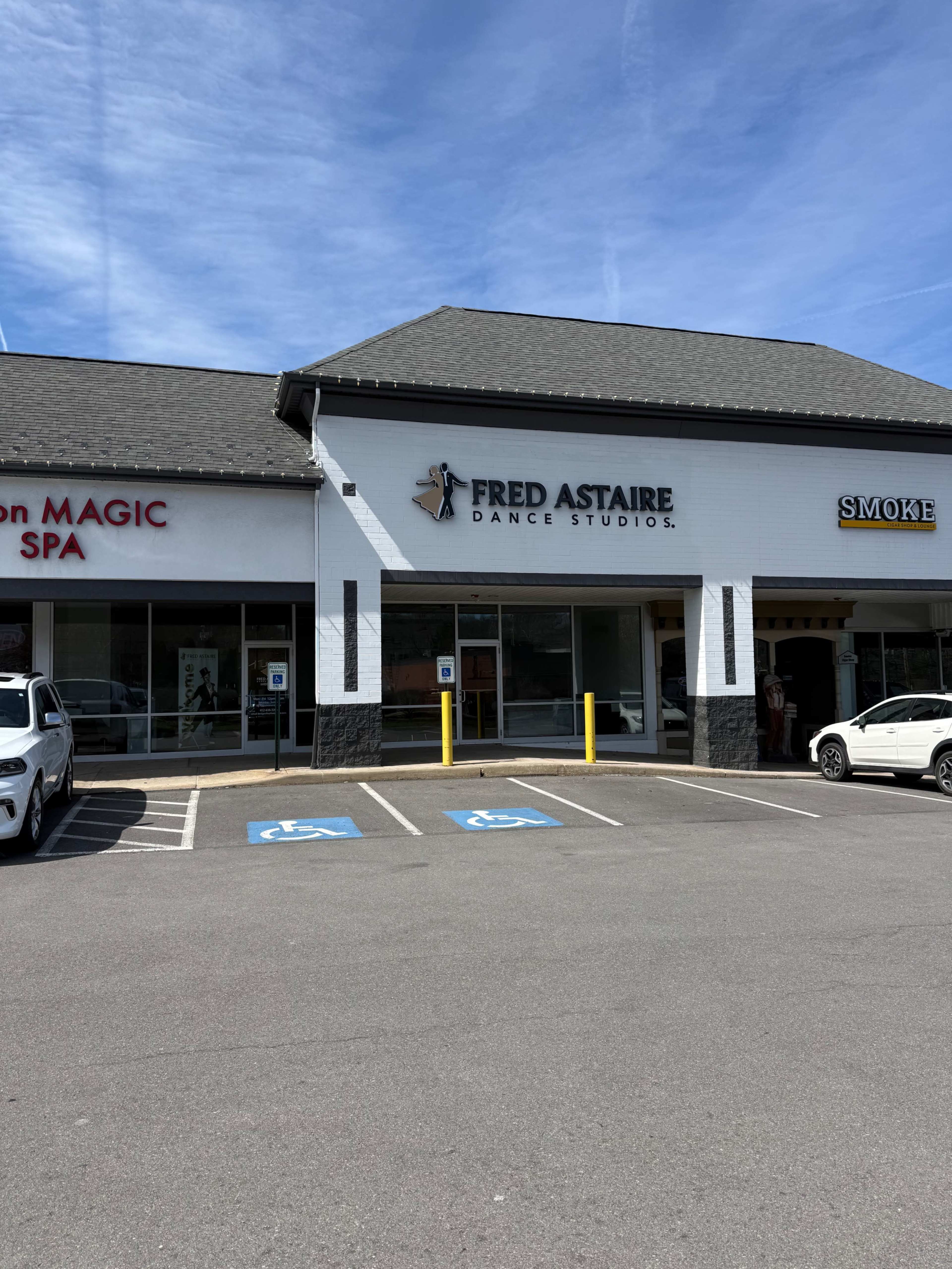 The image shows a shopping plaza featuring the Fred Astaire Dance Studios, located between a magic spa and a smoke shop, with several parked cars in front.