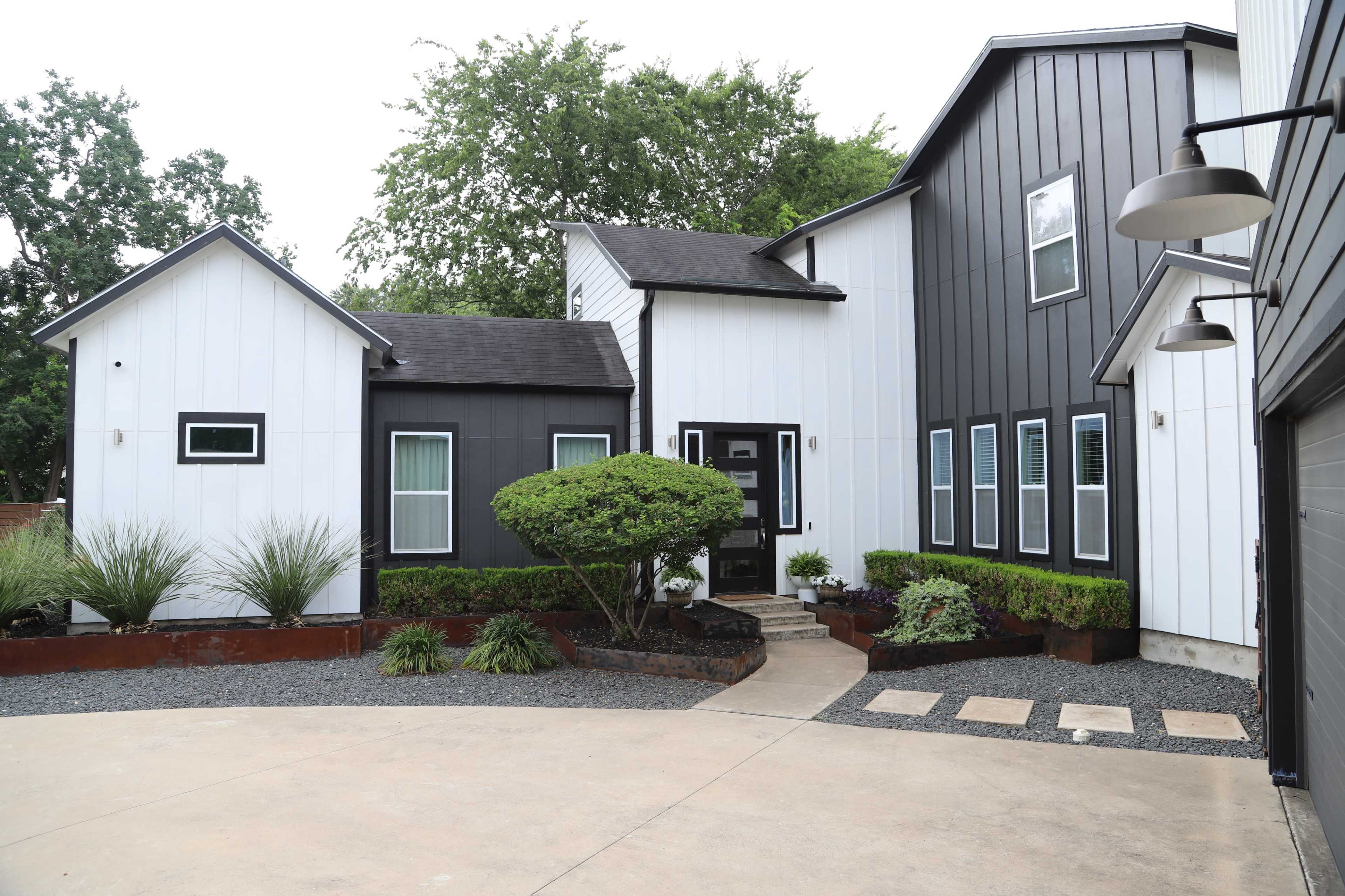 The image features a modern two-story house with a combination of black and white siding, landscaped with shrubs and gravel in the front yard.