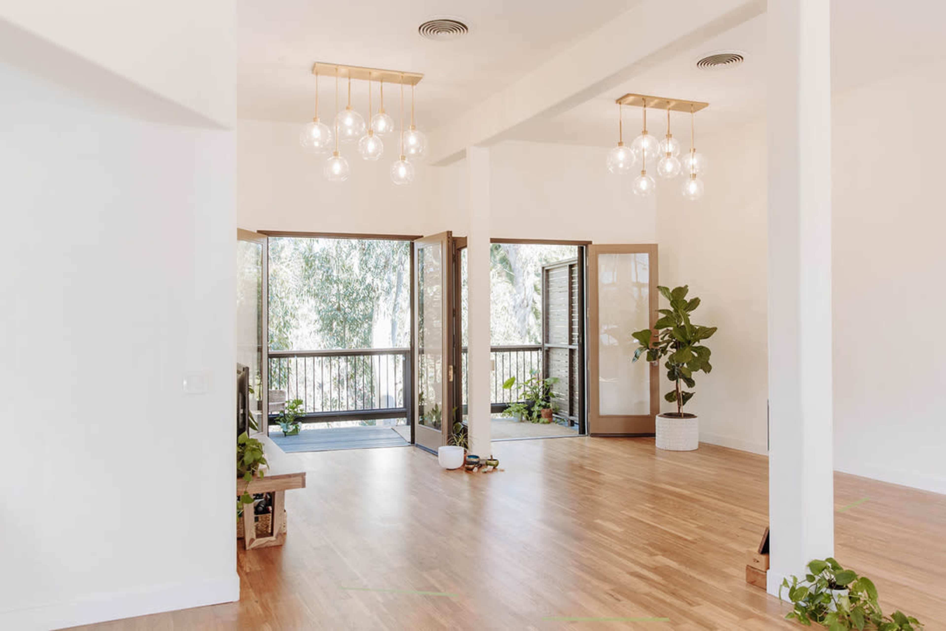 The image shows a bright, open interior space with large windows, wooden flooring, and hanging light fixtures.