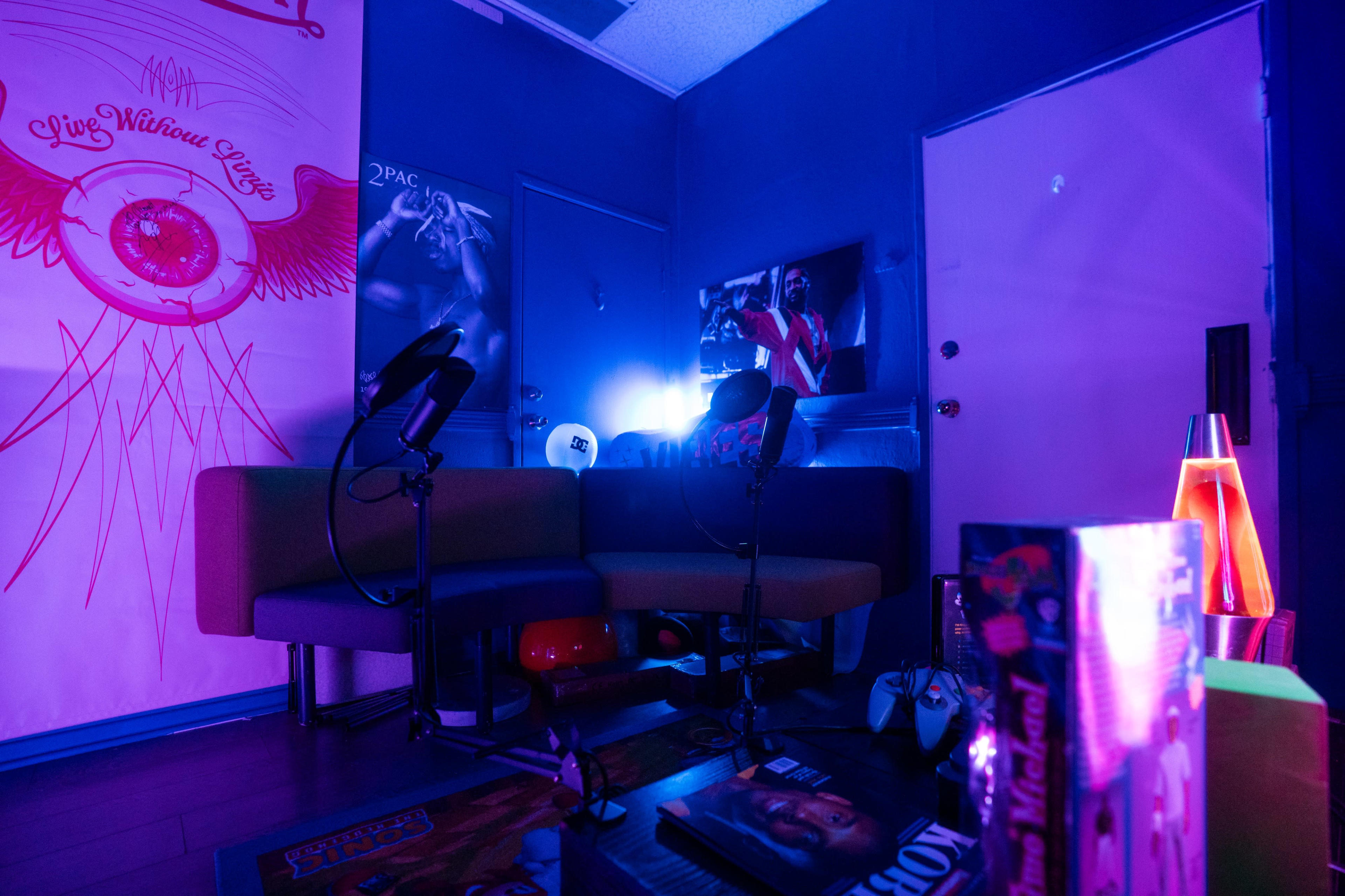 The image shows a vibrant room with colorful lighting, featuring a seating area, microphones, and various posters on the walls.