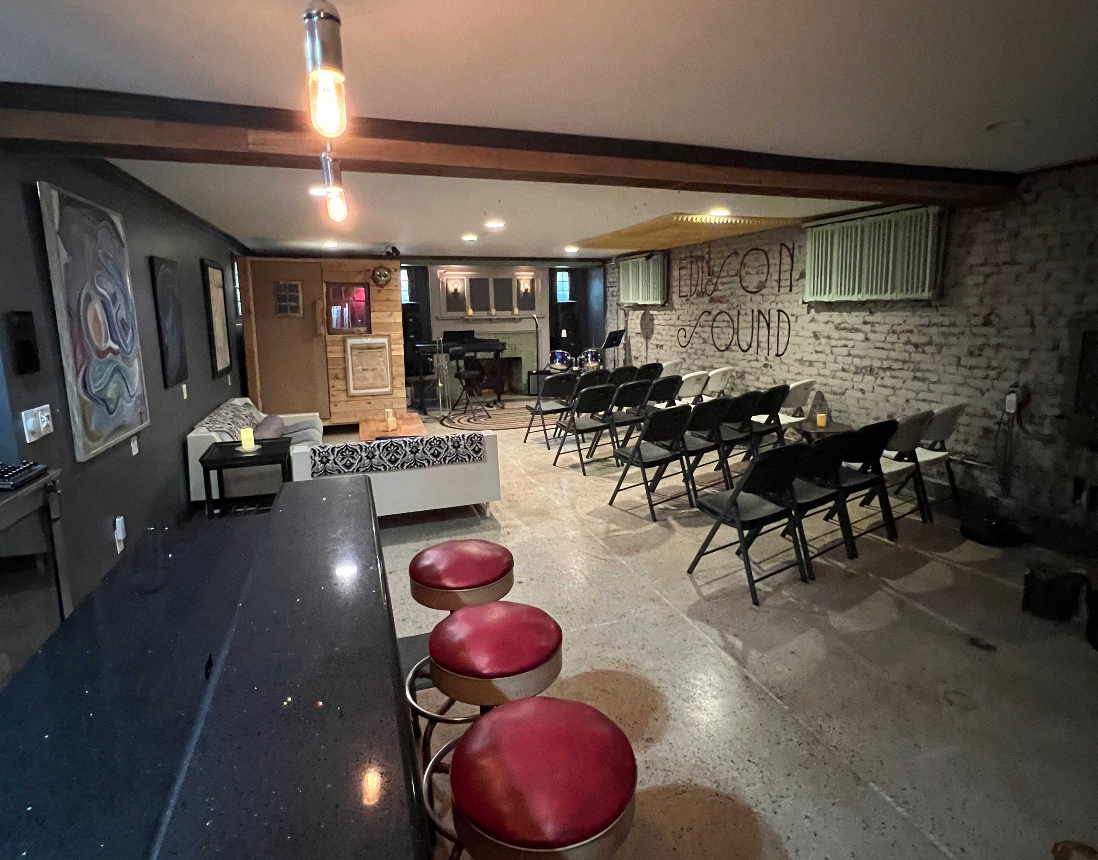 A spacious room with a bar area, seating arranged in rows, and a performance space featuring a microphone and sound equipment.