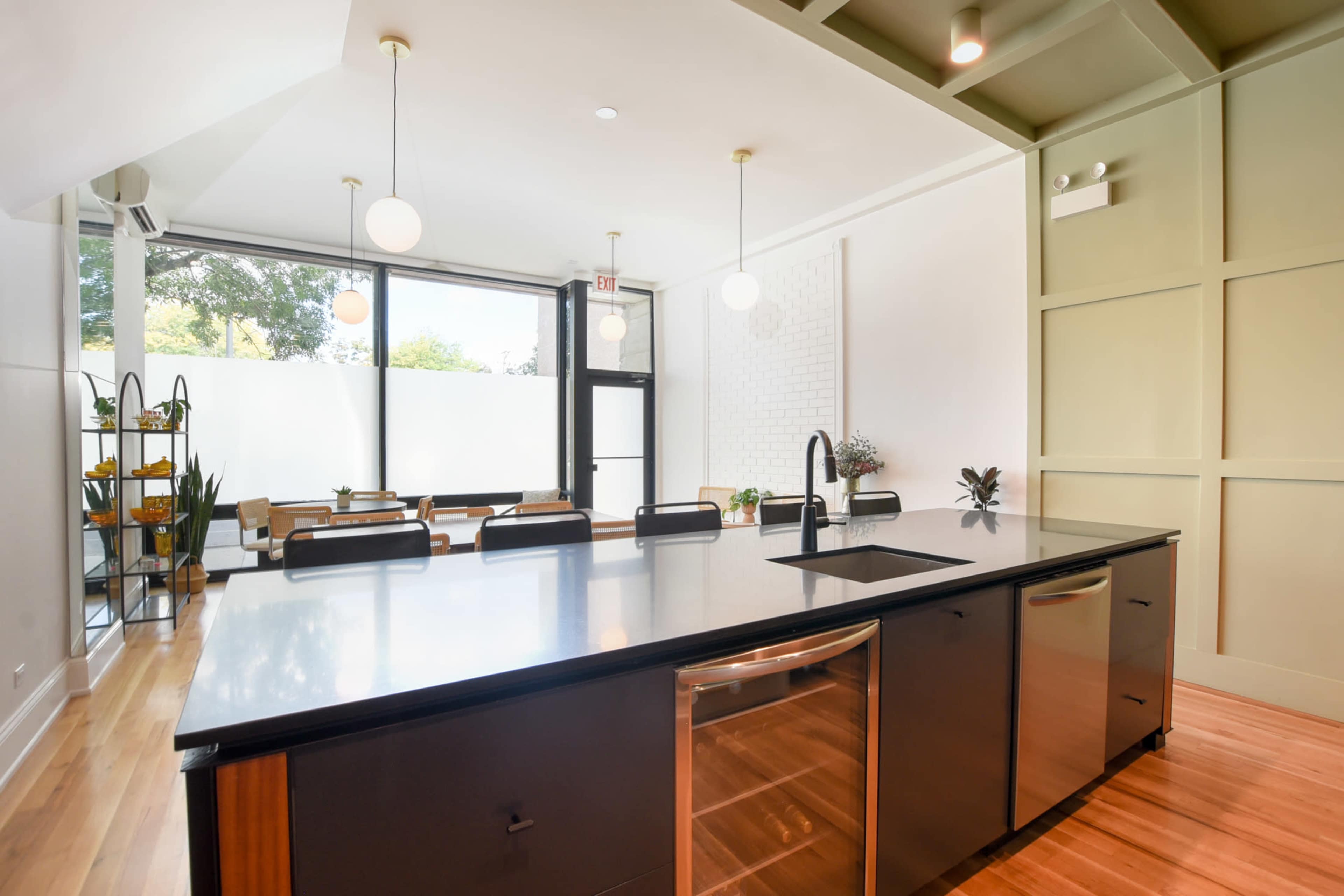 A modern kitchen features a large island with a sink and stainless steel appliances, adjacent to a dining area with large windows and a view of greenery.