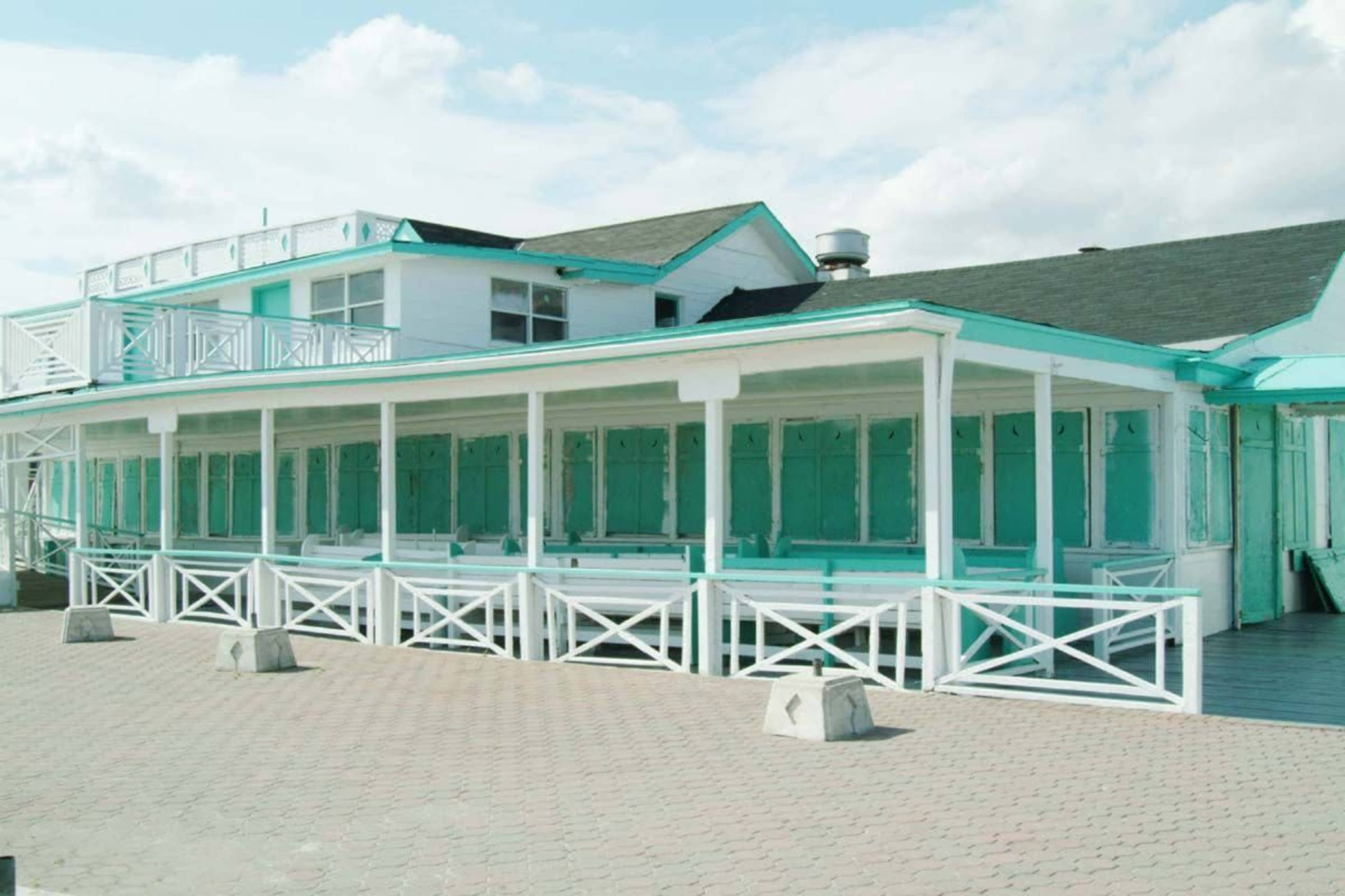 A coastal building with turquoise trim and white wooden structures on a paved surface.