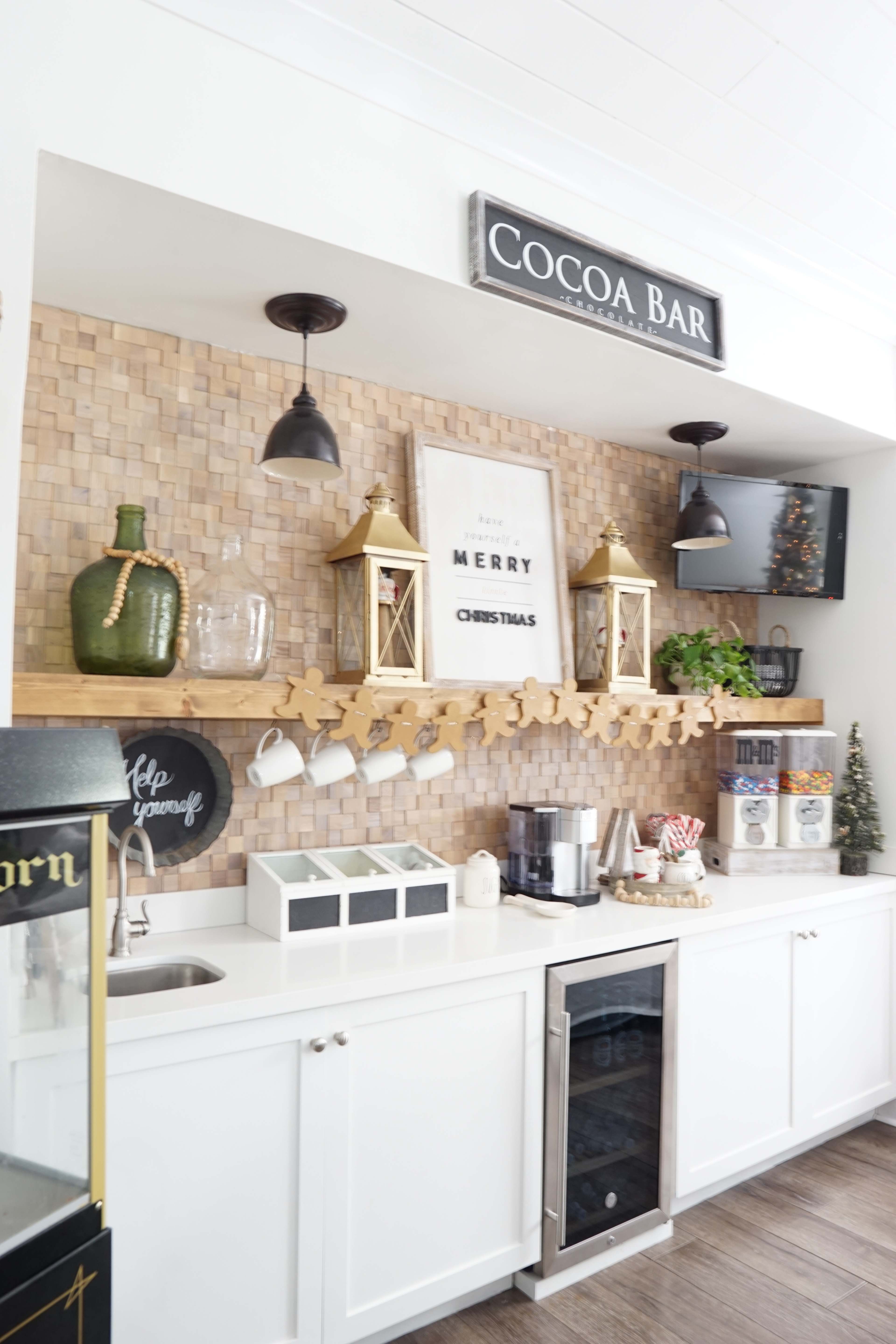 A kitchen area featuring a cocoa bar with decorative lanterns, a wooden shelf, and various containers arranged above a countertop.