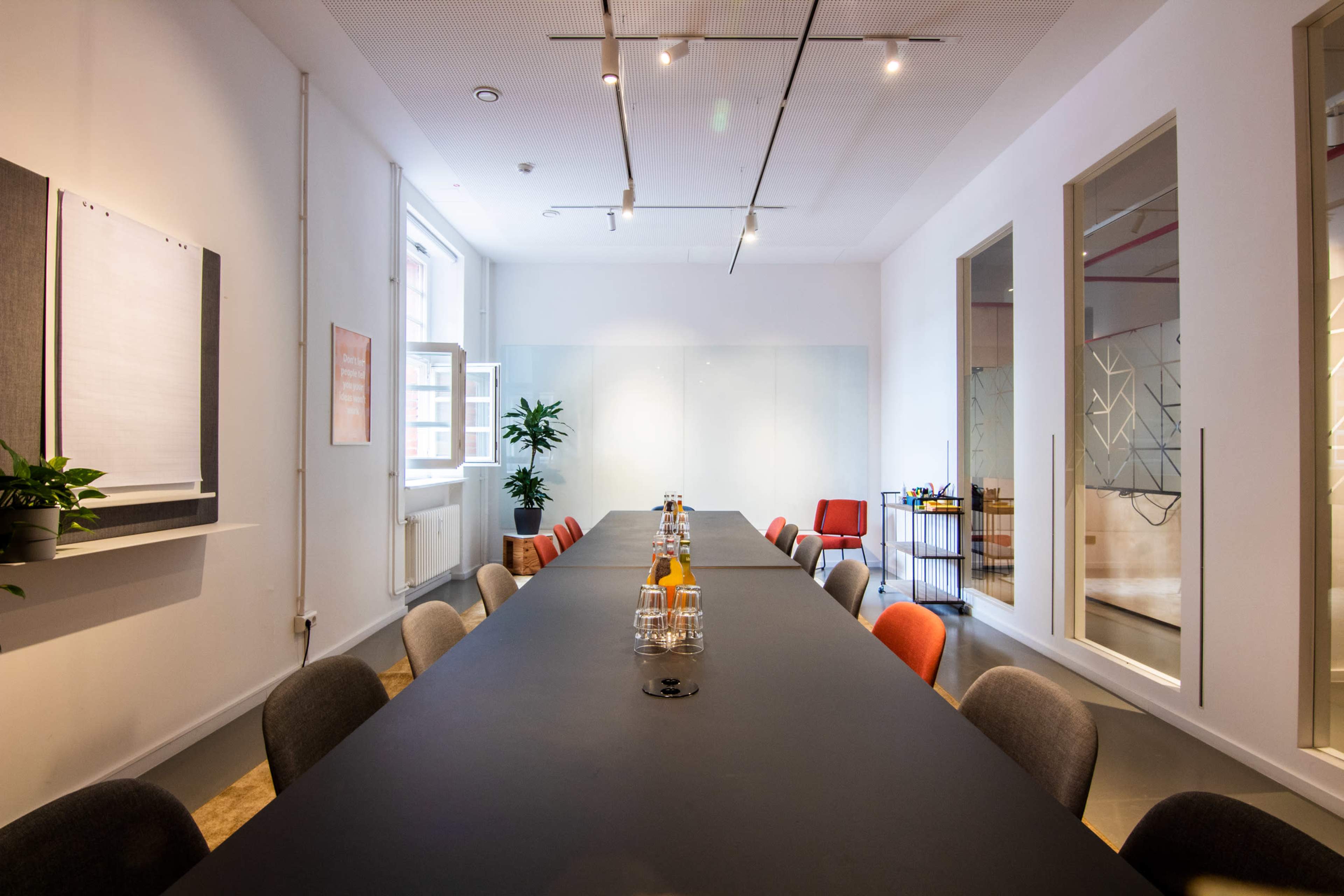 A large meeting room features a long black table with chairs around it and glass walls on either side.