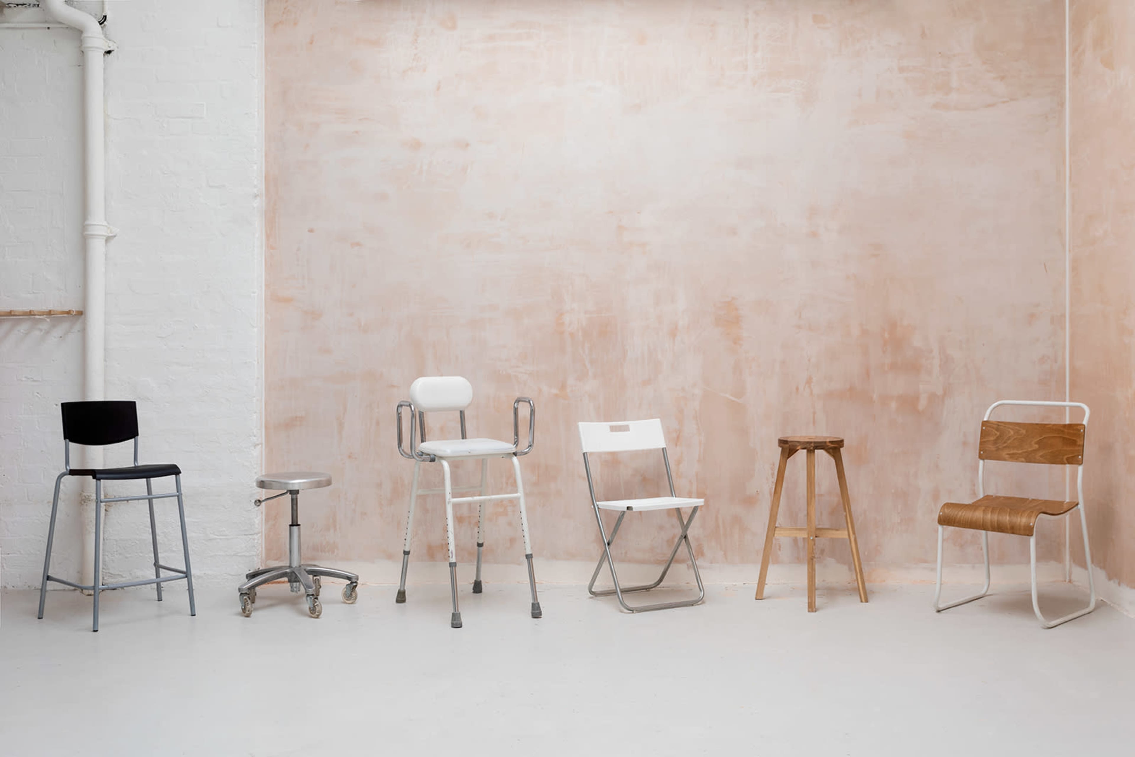 A row of six different chairs against a pale, textured wall in a minimalist setting.