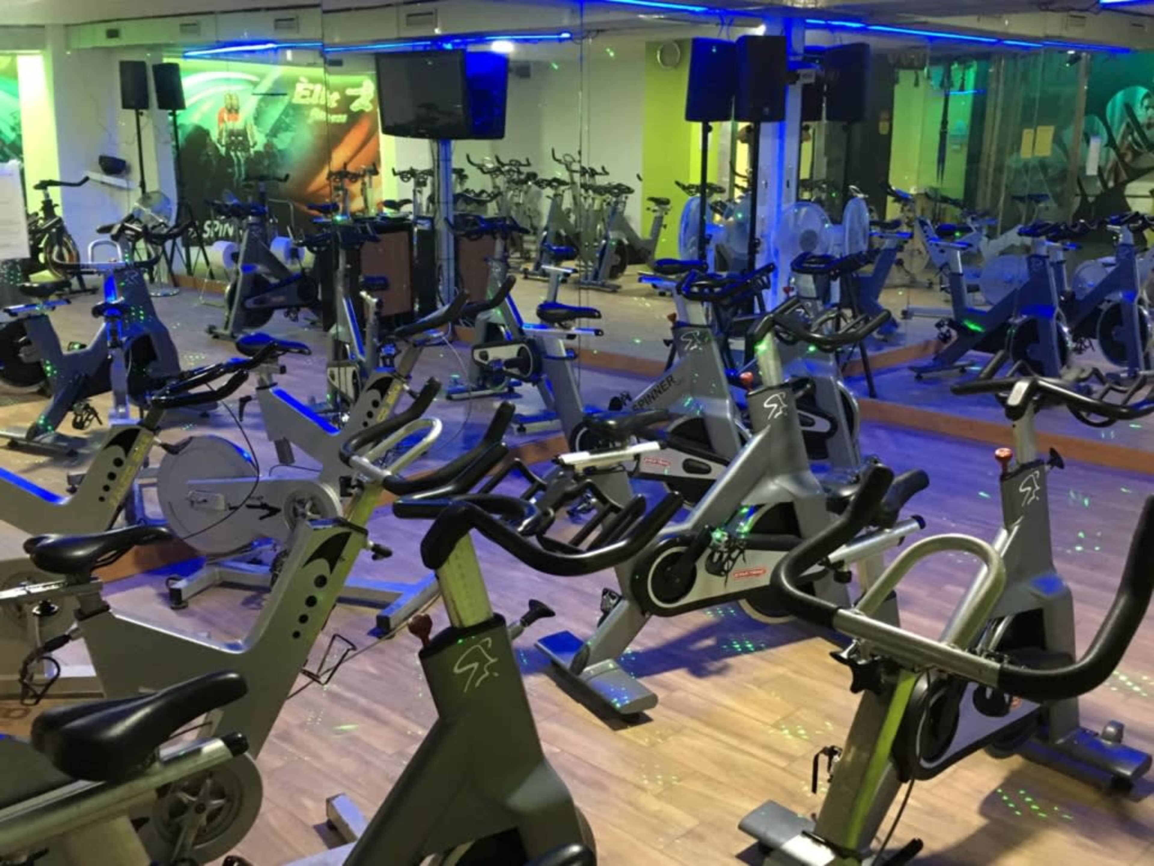 The image shows a spinning studio filled with stationary bikes arranged in rows, illuminated by colorful lights and mirrored walls.