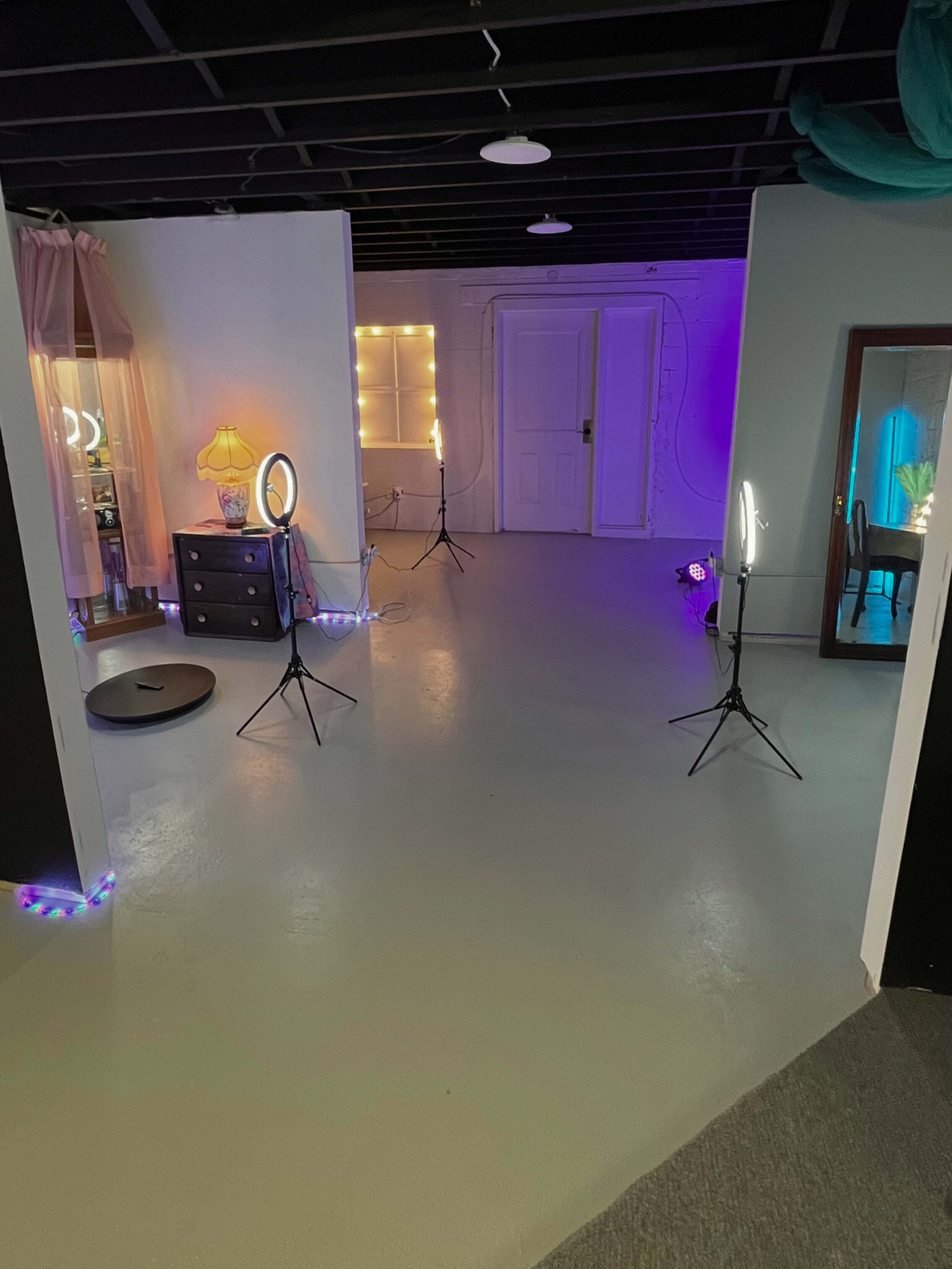 A brightly lit studio space with several lighting setups, a dresser, and a door leading to another room.