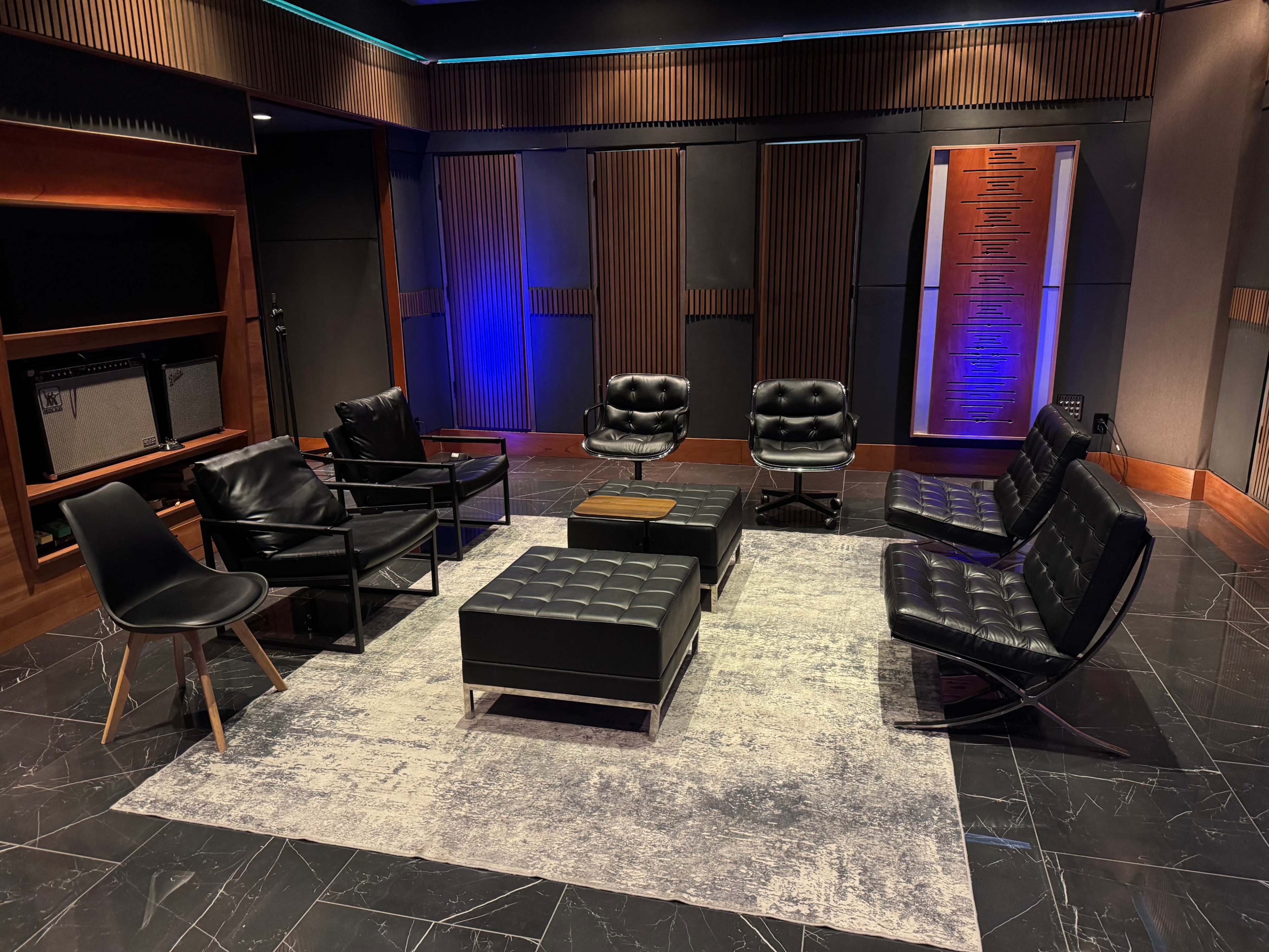 A modern lounge area features black leather chairs and a coffee table on a gray rug, surrounded by wooden paneling and soft lighting.
