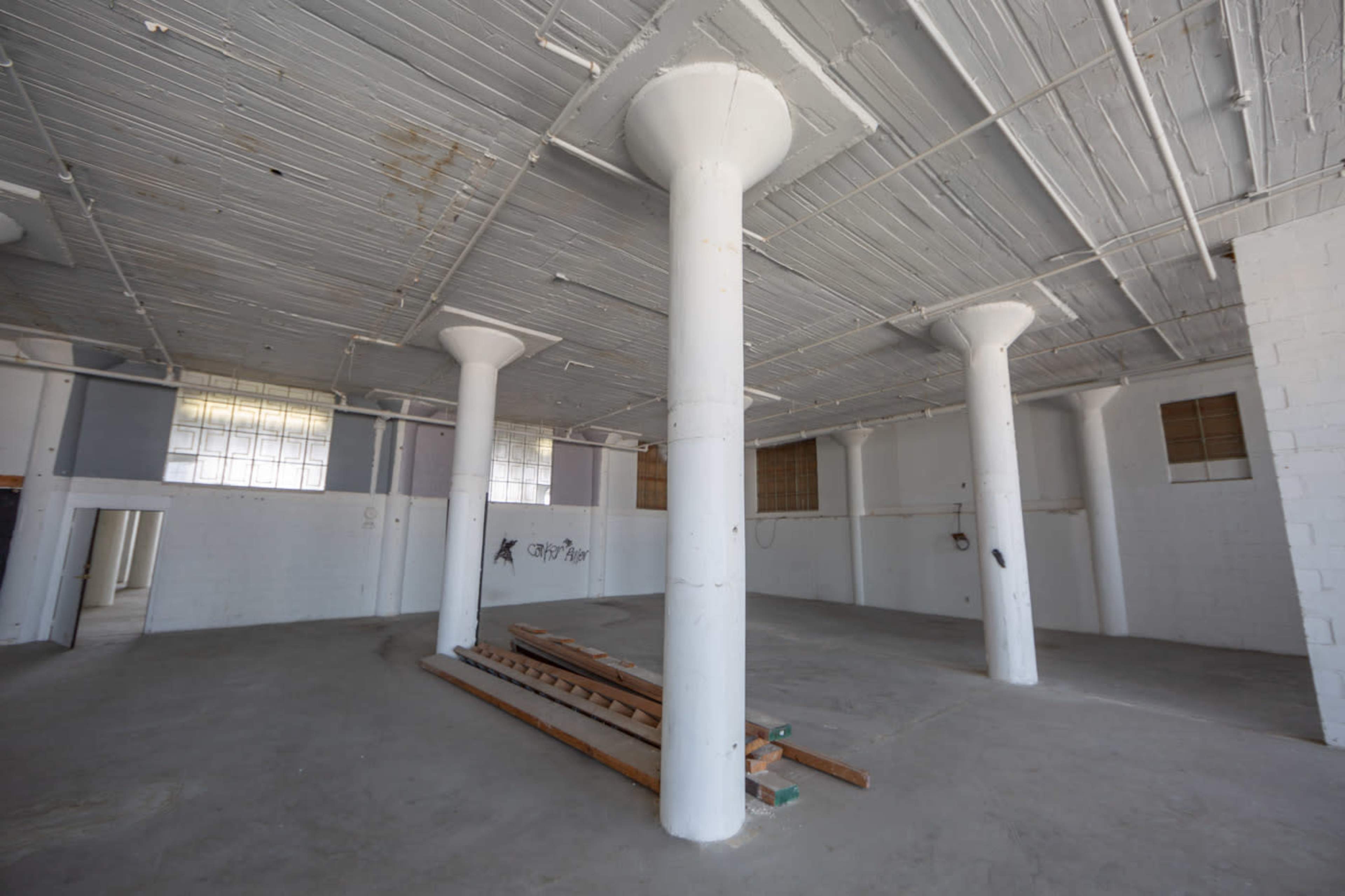 An empty room with multiple white columns stands on a concrete floor, featuring sparse natural light from large windows.